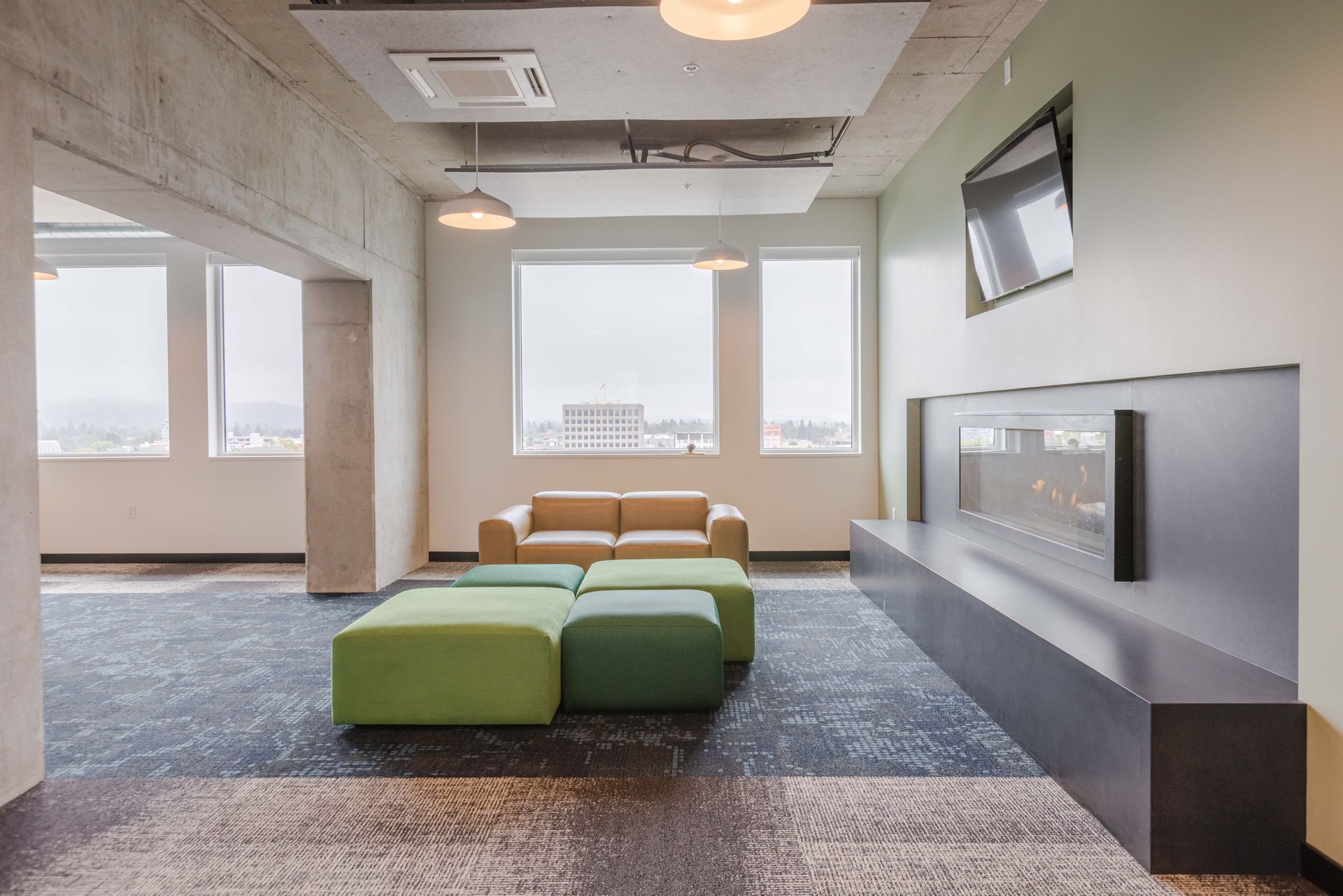 Modern lounge with green and tan seating, large windows, and a gray wall-mounted fireplace.