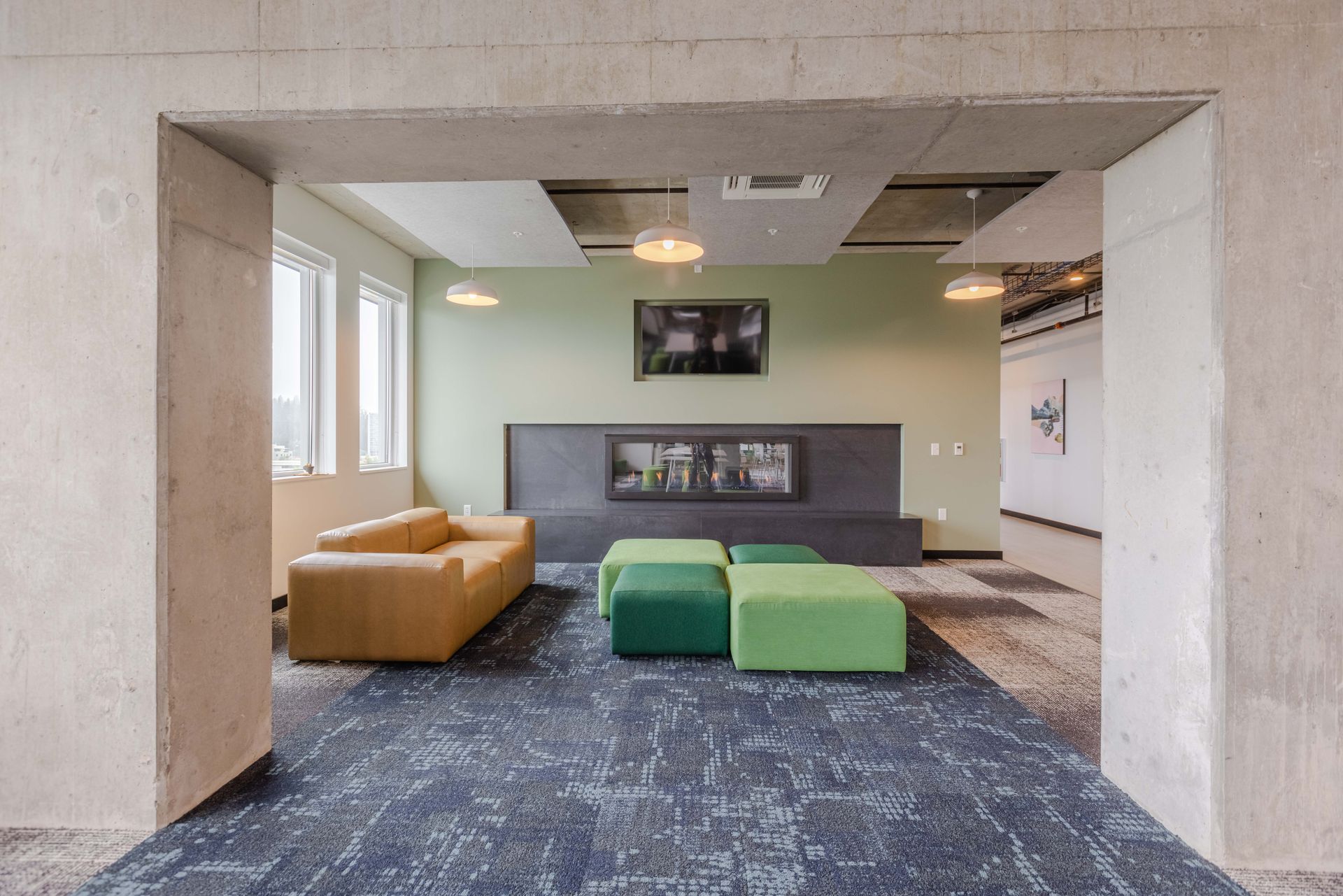 Modern lounge with green and orange modular seating, patterned carpet, and wall-mounted TV in a bright room