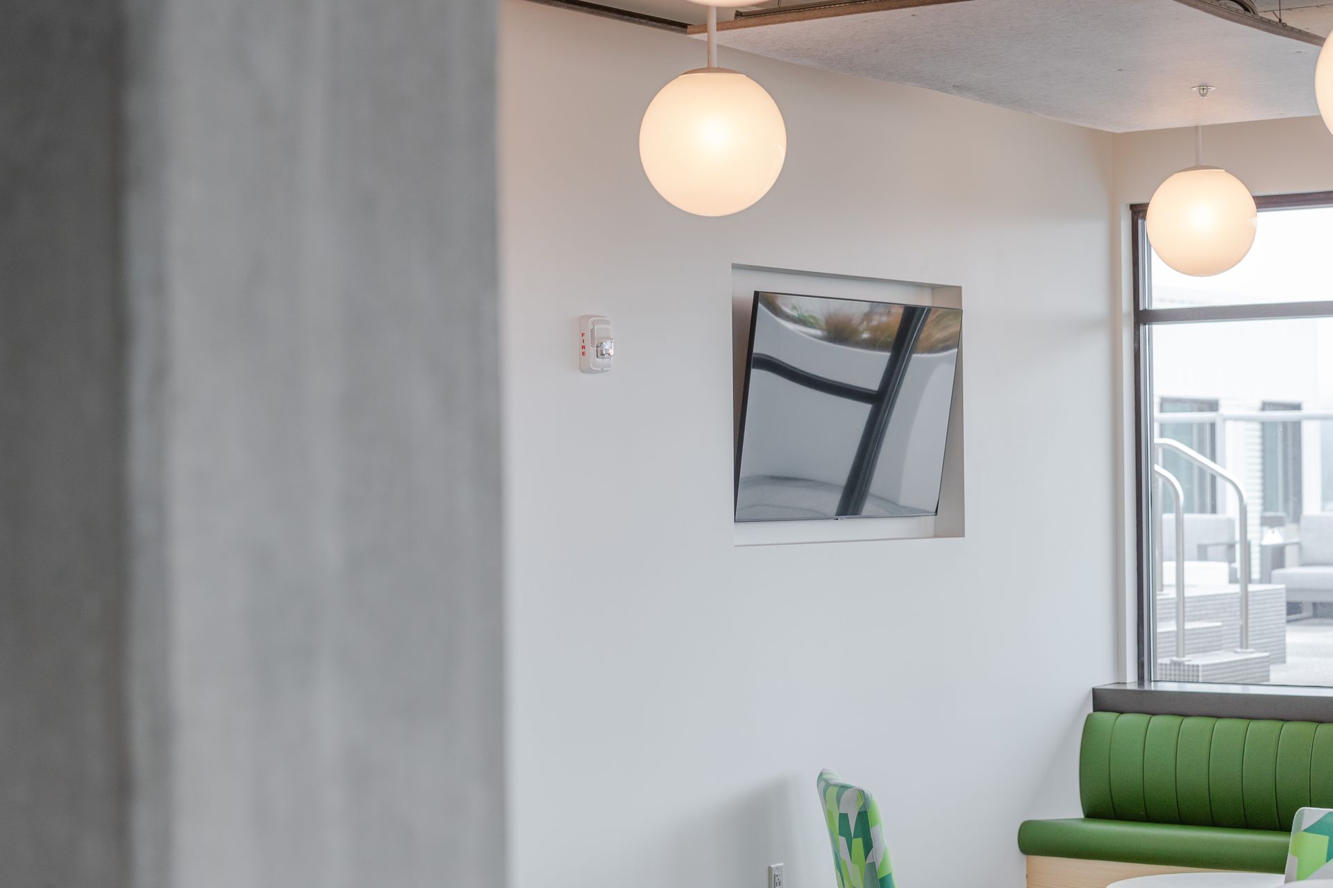 Modern lounge with white walls, hanging globe lights, a framed picture, and a green sofa near a window.