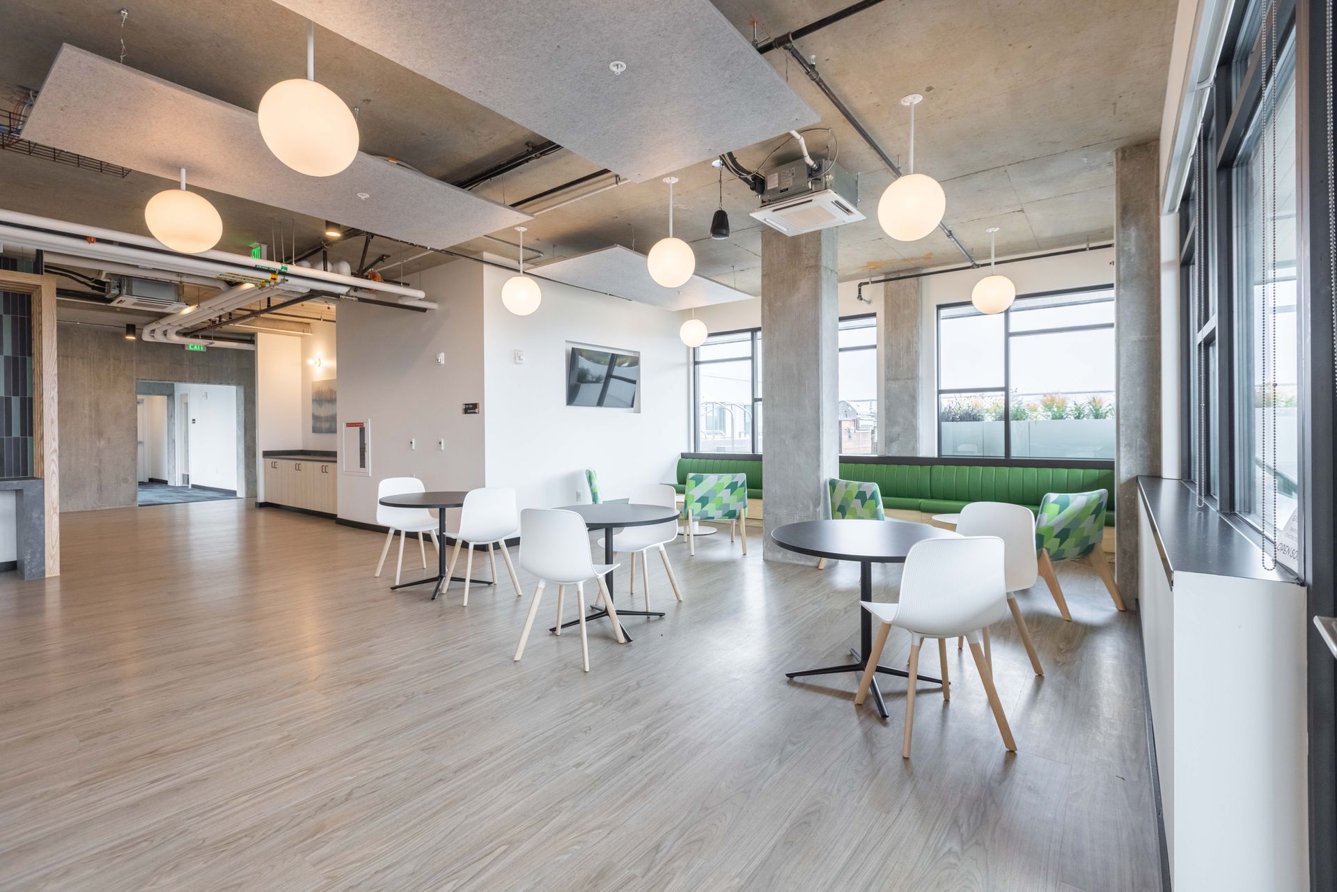 Bright modern office lounge with white chairs, round tables, large windows, and hanging globe lights