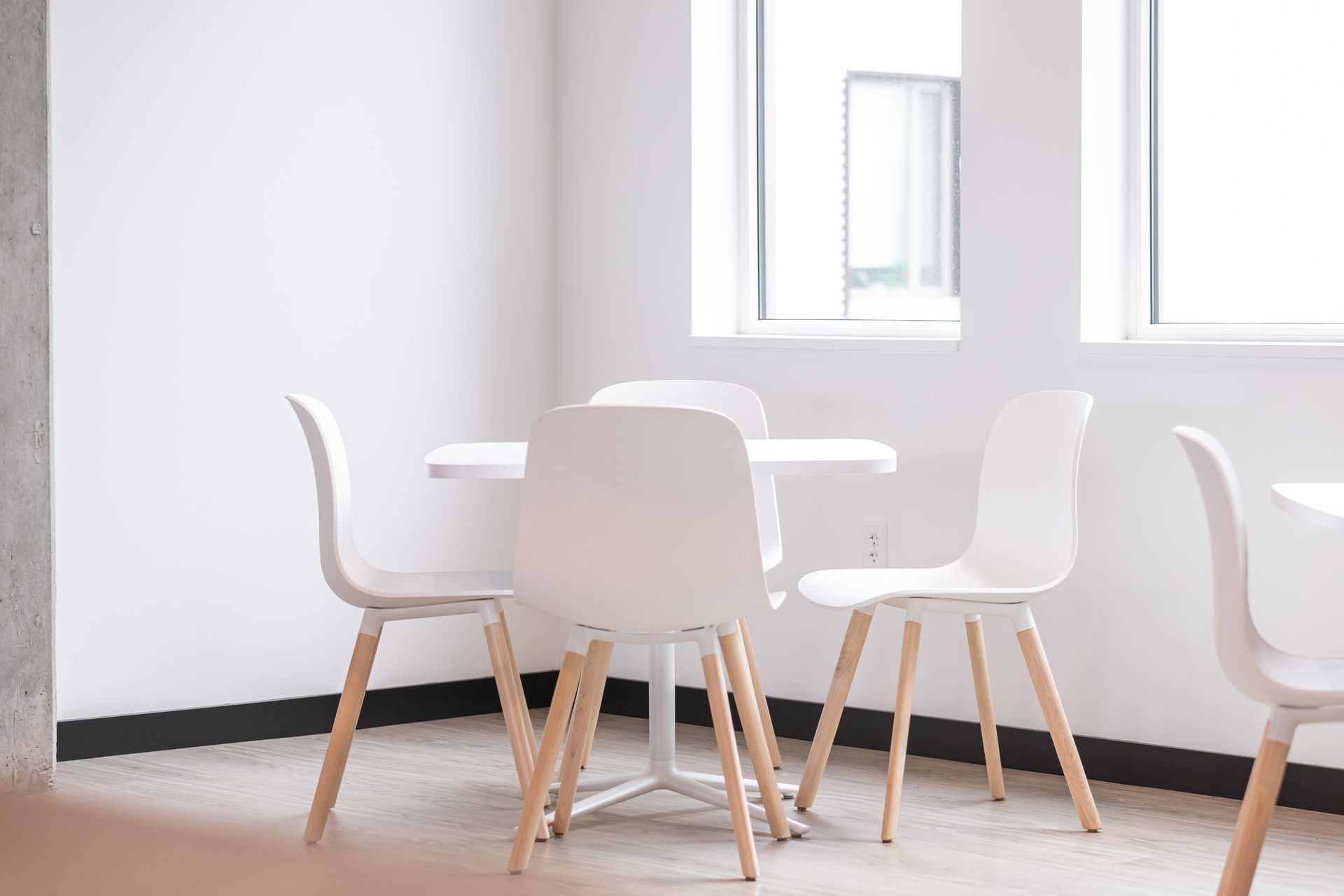 Bright dining area with white chairs around a table near large windows