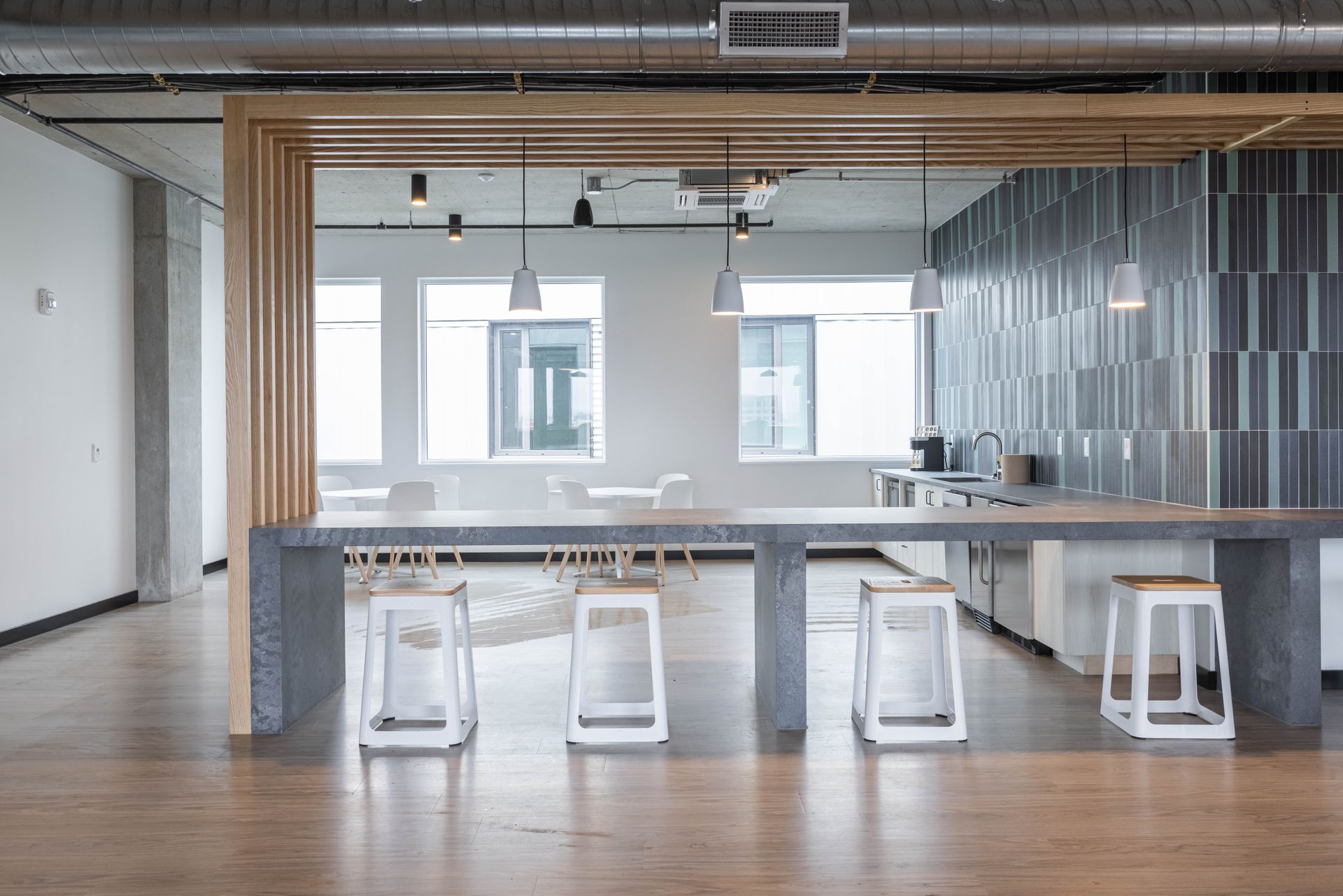 Modern open-plan office with wooden table, white stools, and large windows