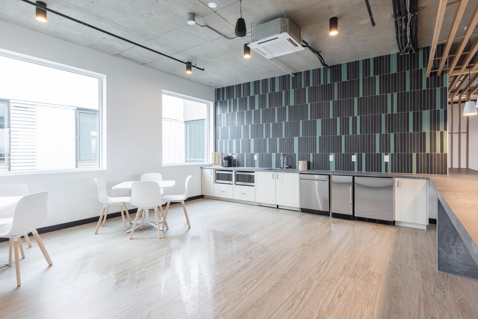 Modern open-plan kitchen and dining area with white furniture, wood floor, and dark tiled accent wall