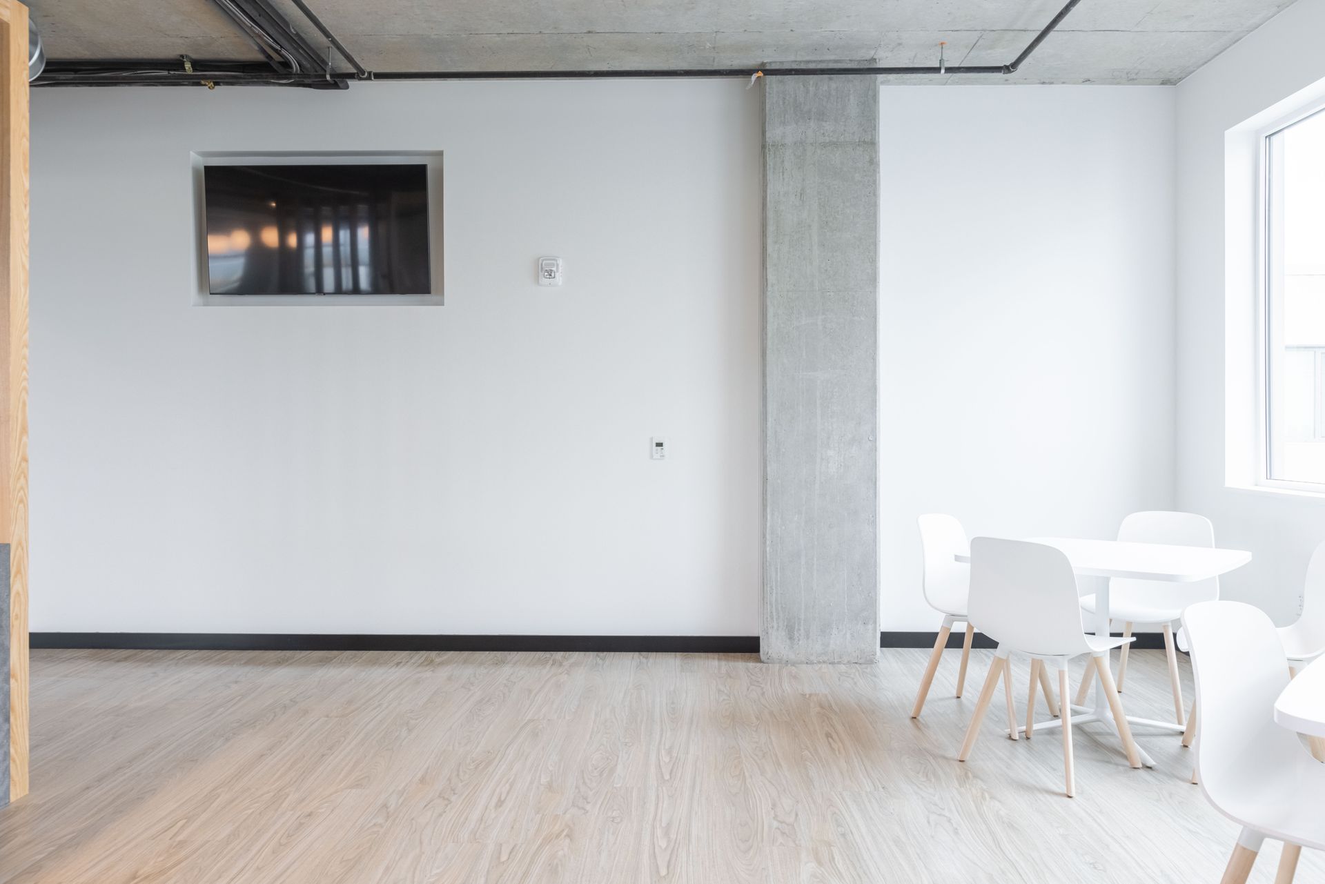 Empty modern room with white chairs, light wood floor, and a wall-mounted screen.