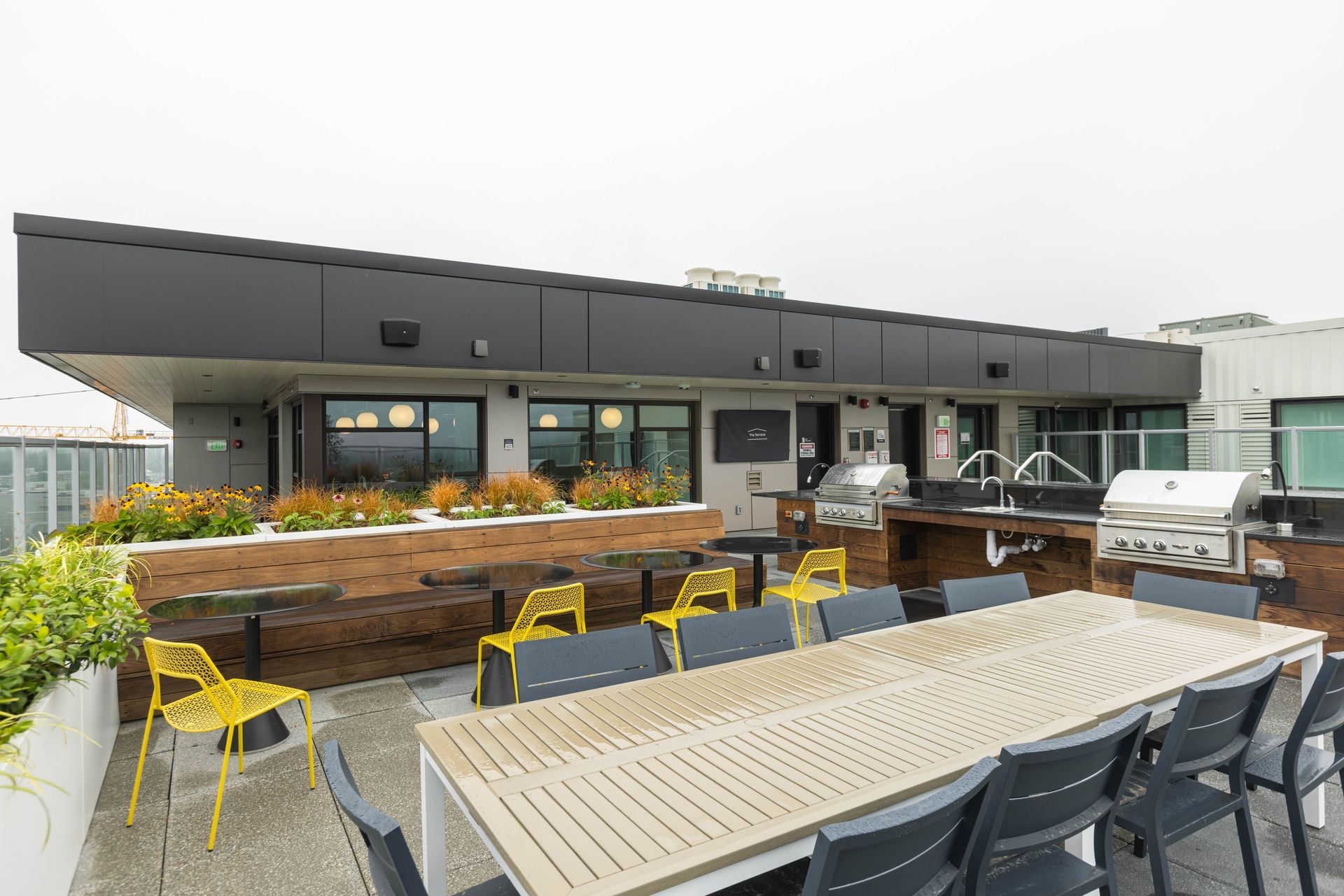 Outdoor rooftop patio with tables, chairs, and a grill beside a modern building