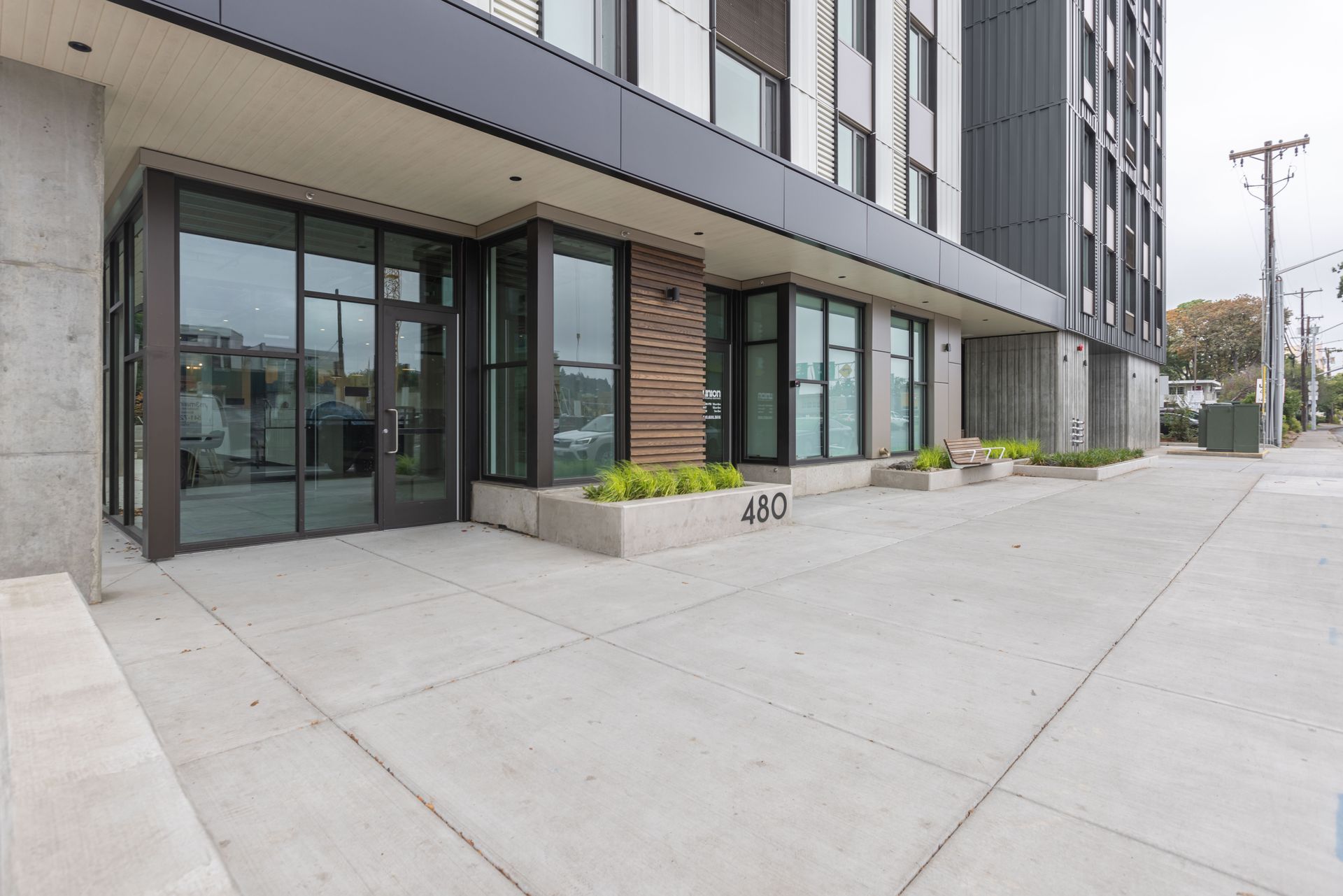 Apartment building entrance with glass doors, sidewalk, and planters along the street.