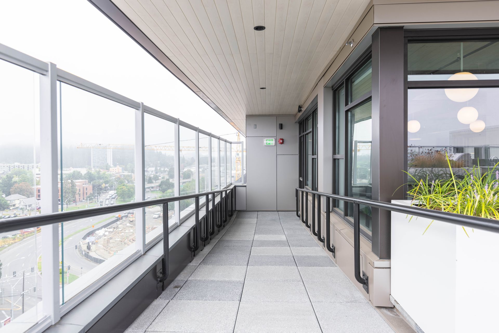 Modern balcony walkway with glass railings, gray floor, and city view beyond