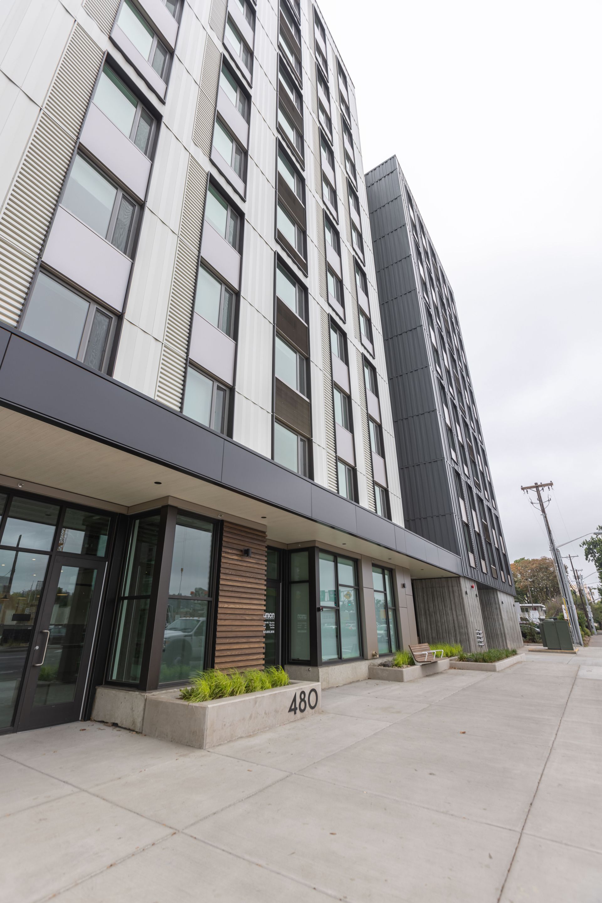 Modern apartment building entrance with glass storefronts and a sidewalk on an overcast day