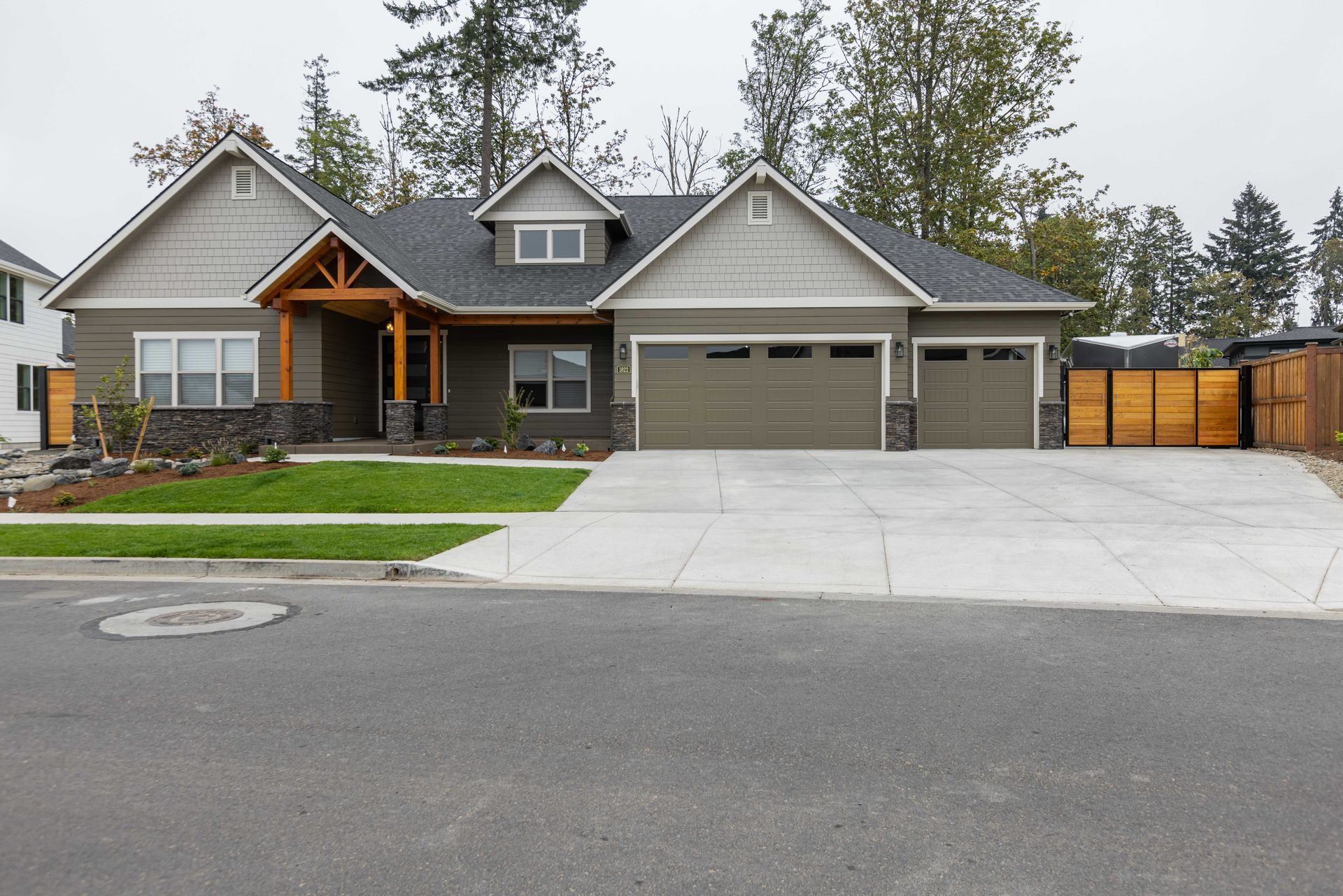 Modern gray house with attached garage and large concrete driveway on a quiet street