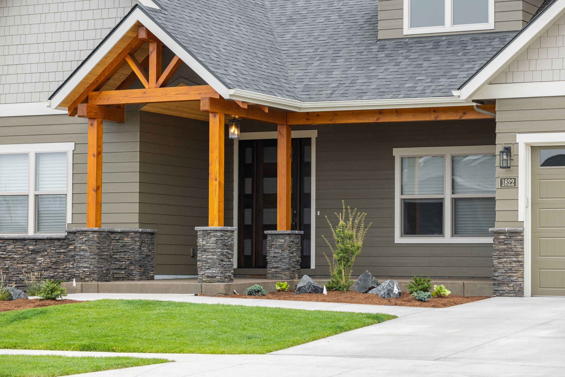 Modern gray house exterior with stone columns, wooden porch, and green lawn