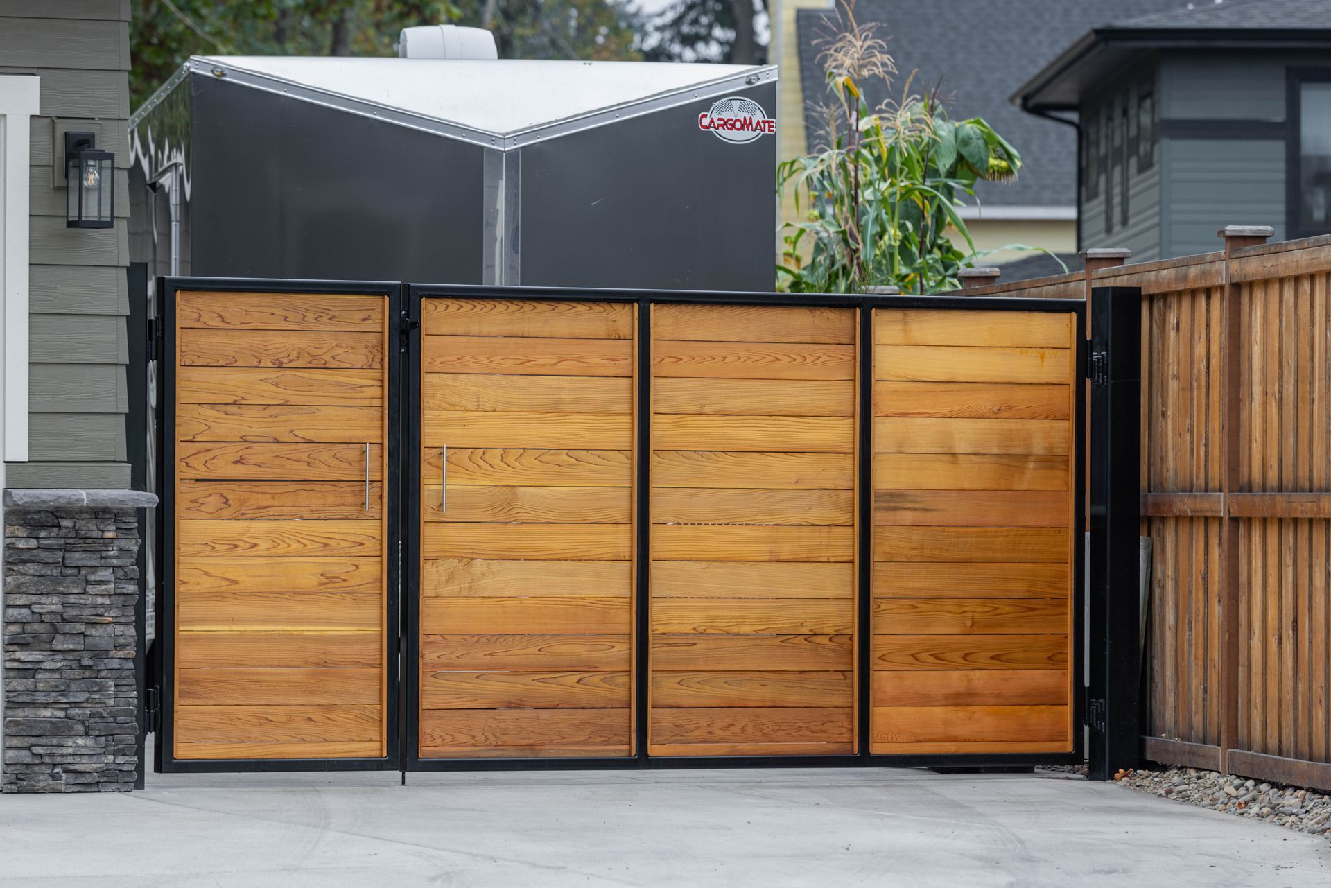 Wooden slat driveway gate with black metal frame in a residential driveway