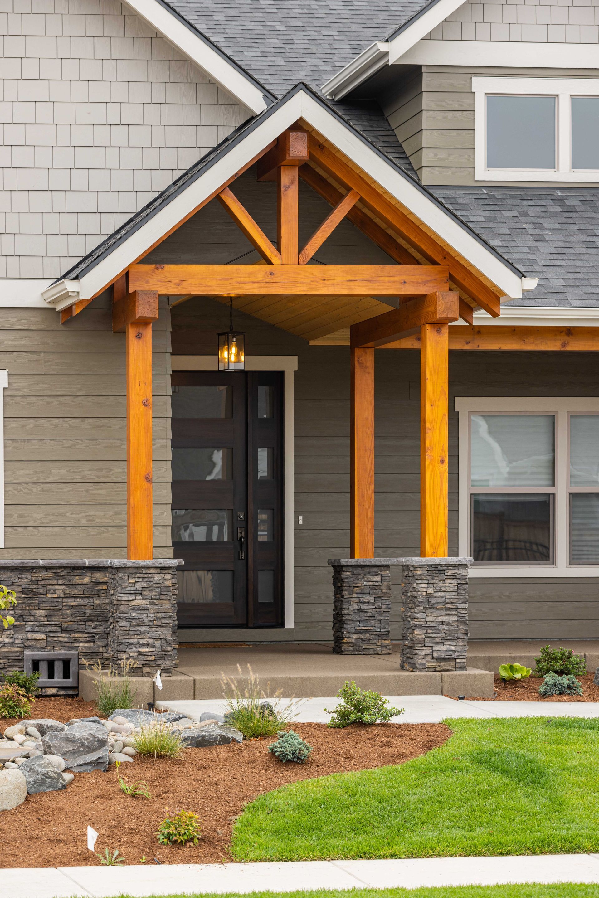 Front entrance of a modern house with wood beams, stone columns, and landscaped yard