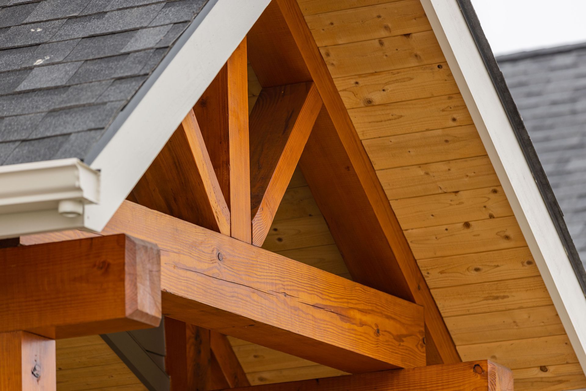 Wooden roof truss and eaves of a house with gray shingles and siding trim