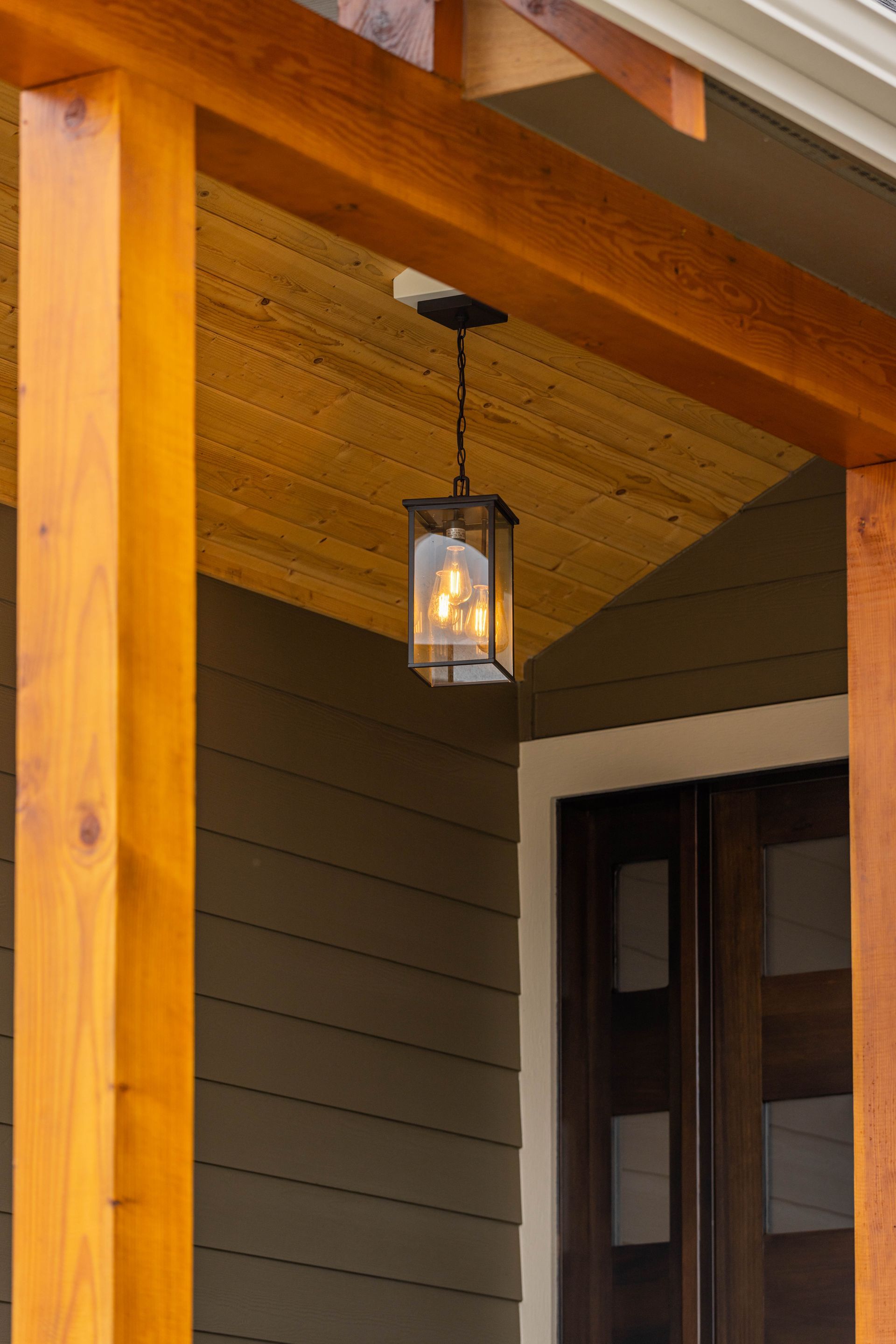 Lantern-style porch light hanging under a wooden entryway ceiling