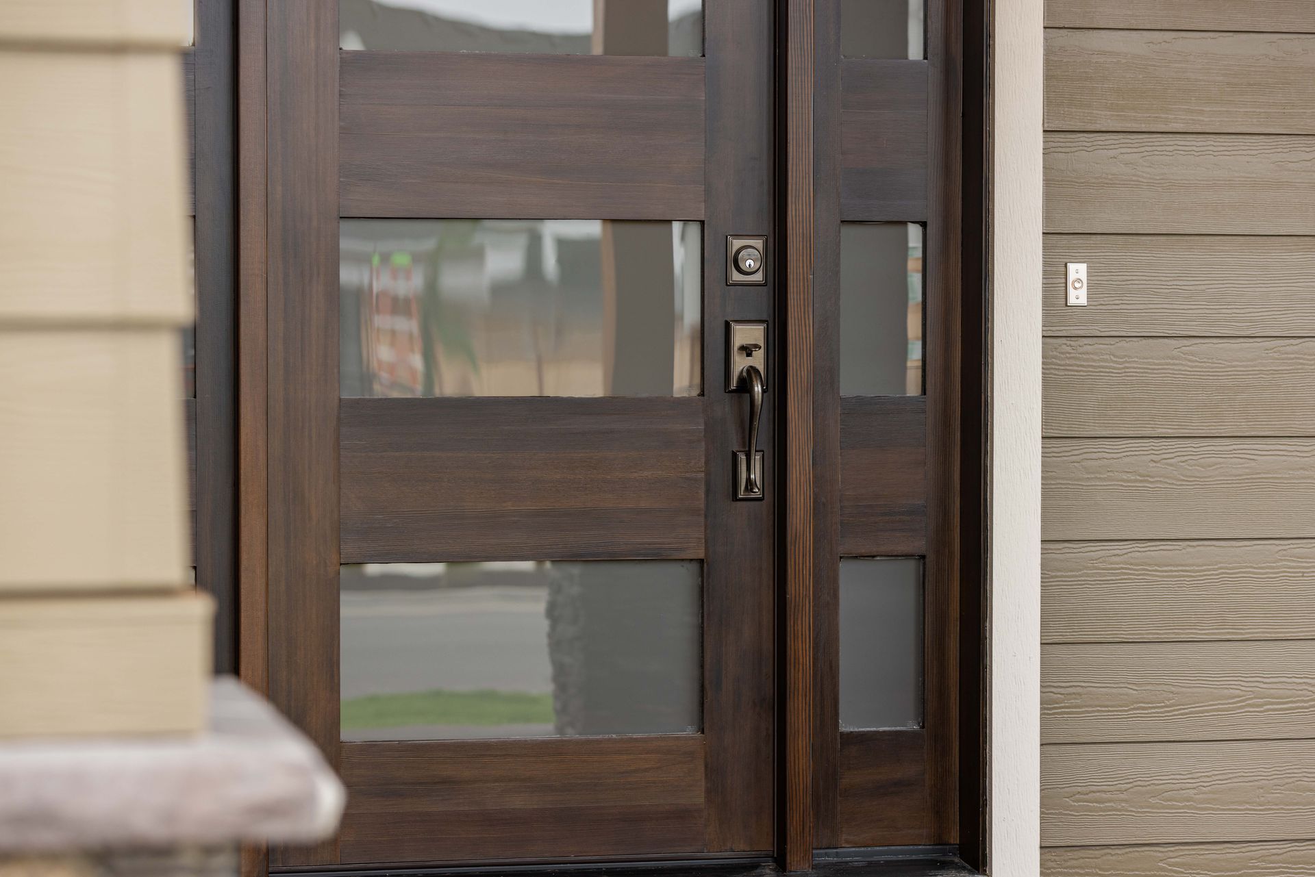 Modern wood-and-glass front door with a black handle and beige siding beside it