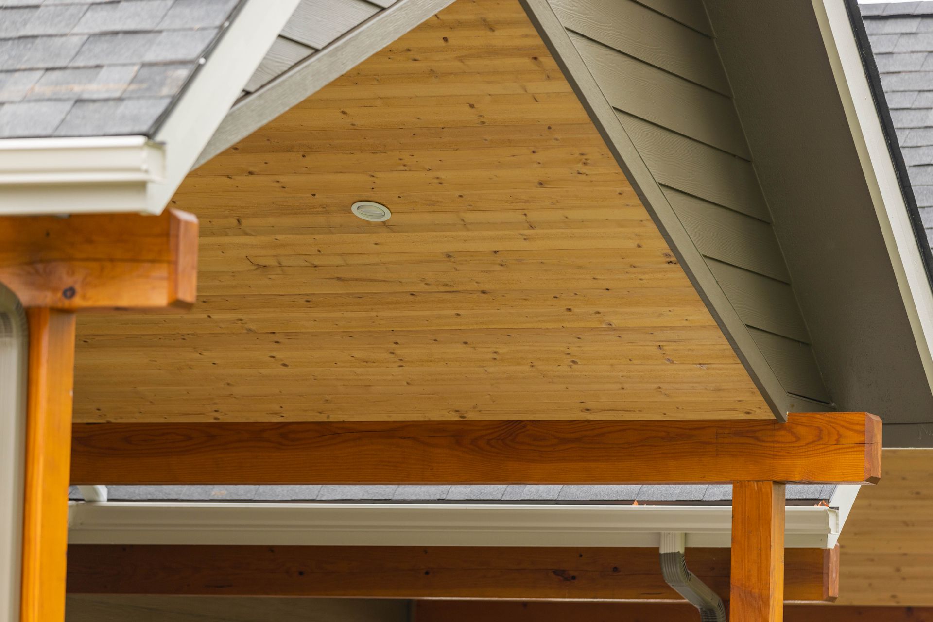 Wooden attic gable with white trim and exposed beams under a shingled roof.