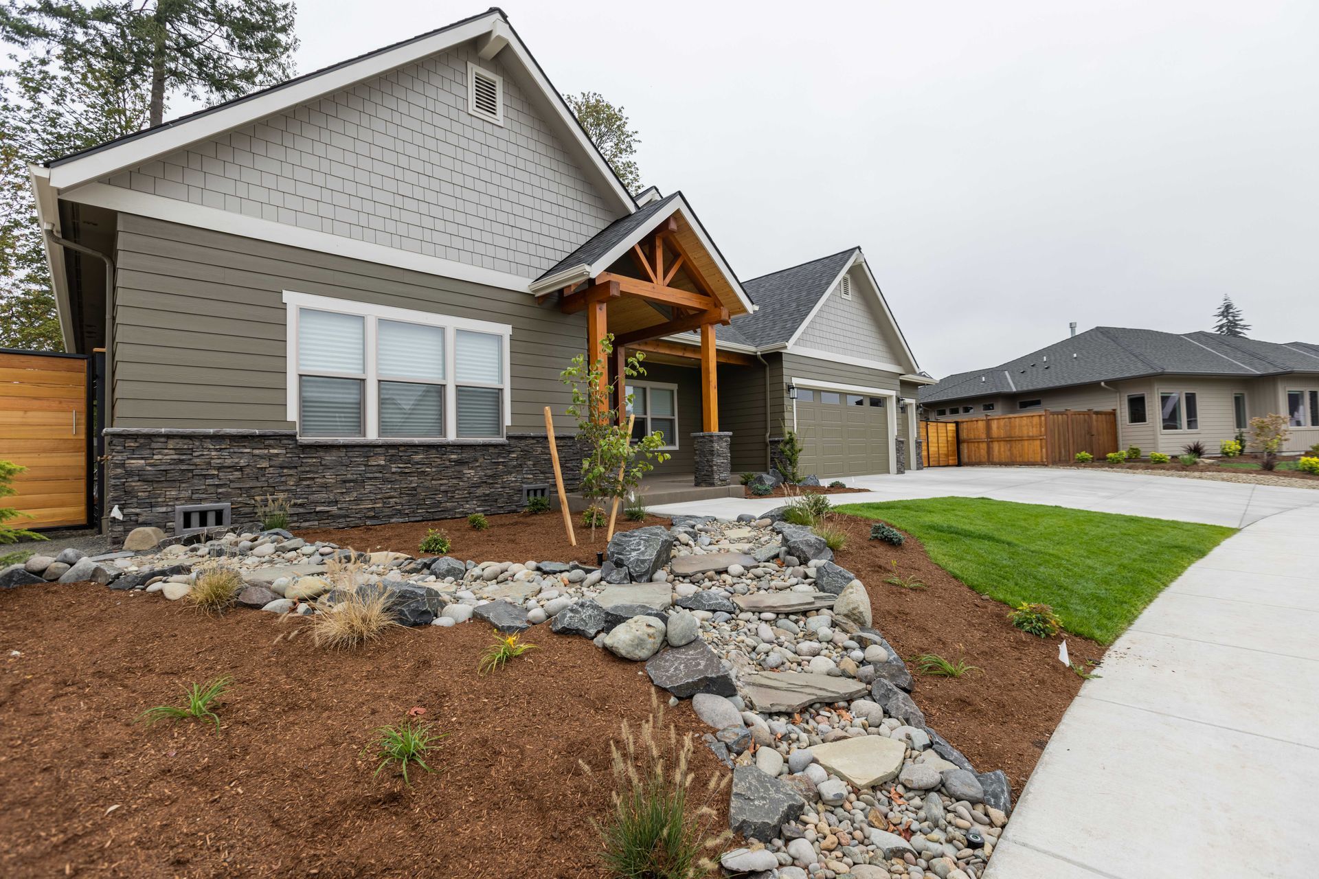 Modern suburban houses with stone landscaping, a front walkway, and a curved sidewalk on a cloudy day