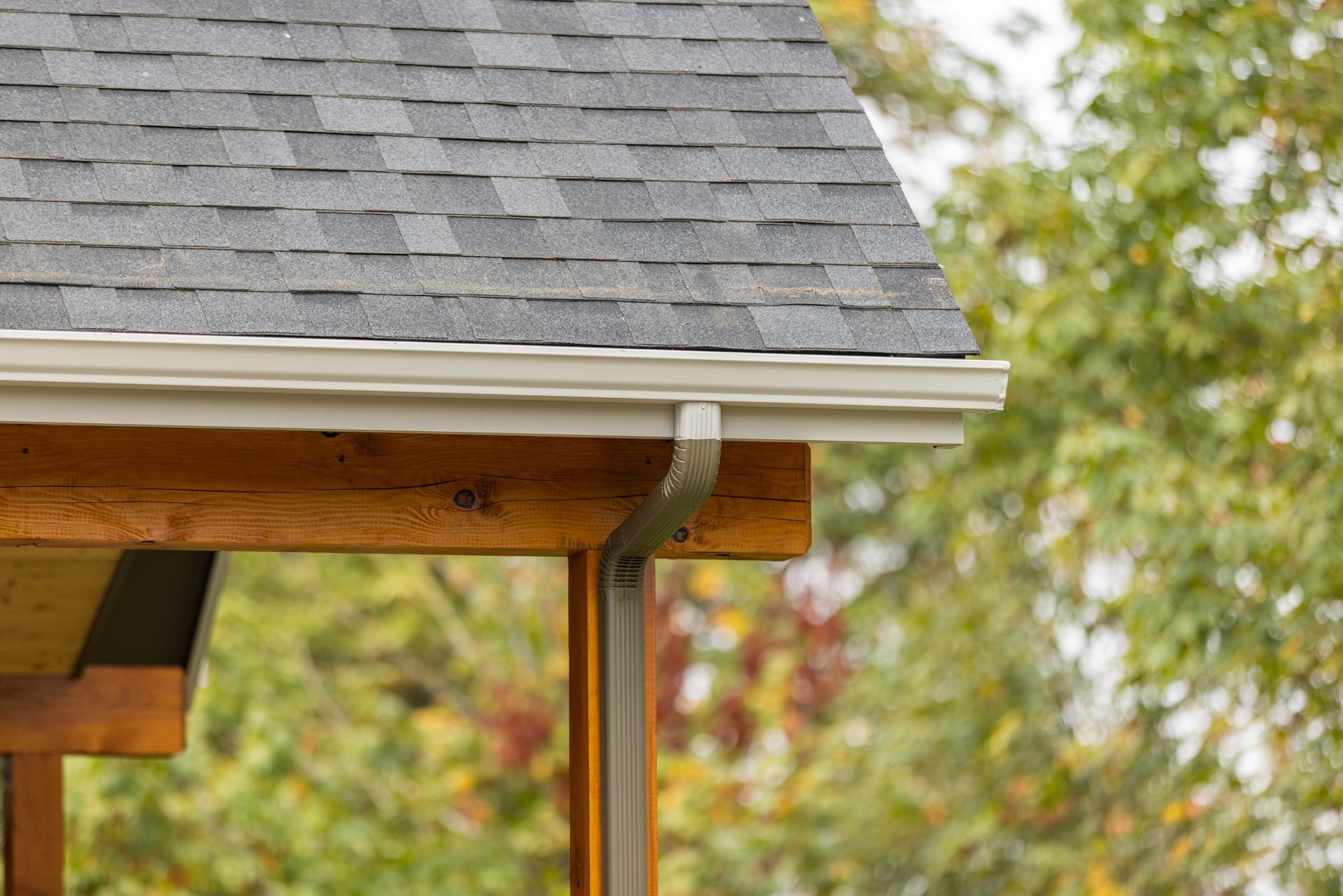 Shingled roof edge and wooden porch post with gutter, outdoors in autumn foliage