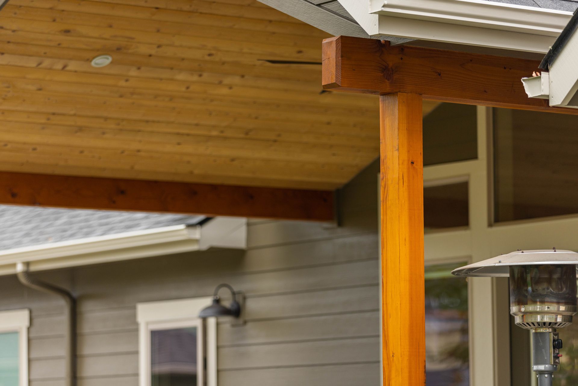 Wooden porch beam and post supporting a roof overhang beside a house exterior.