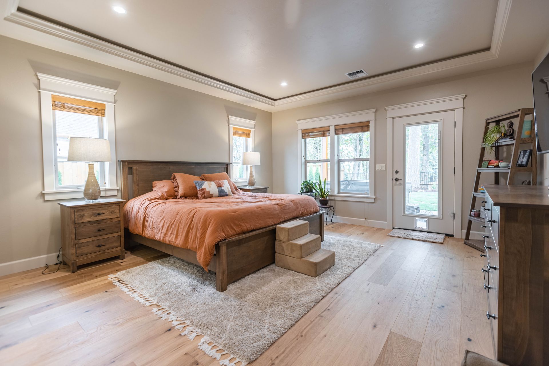 Bright bedroom with wood bed, orange bedding, rug, dresser, and large windows with a glass door