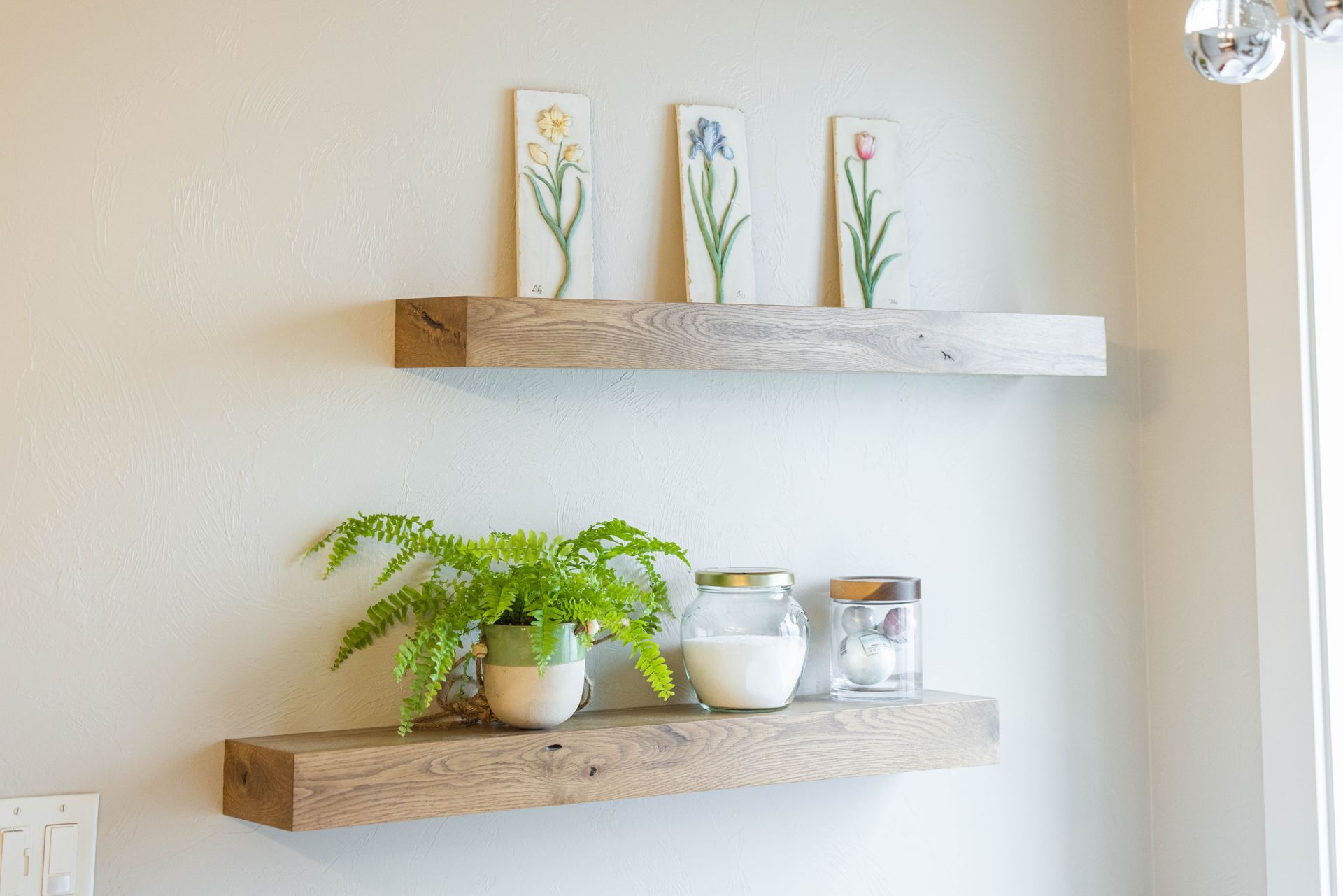 Minimal wall shelf decor with potted fern, jars, and small floral art on a white wall