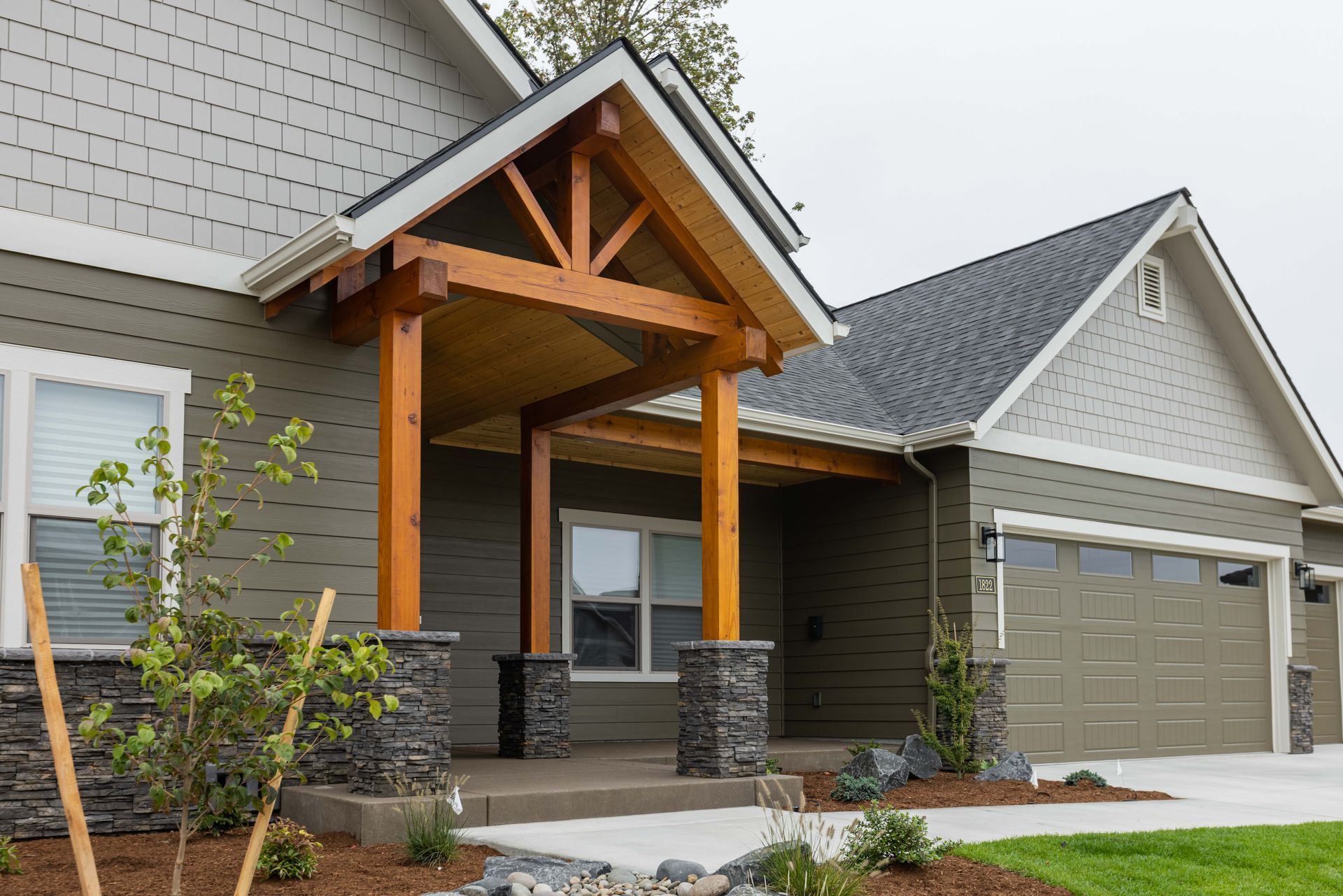 Suburban house exterior with gray siding, stone porch columns, and a two-car garage