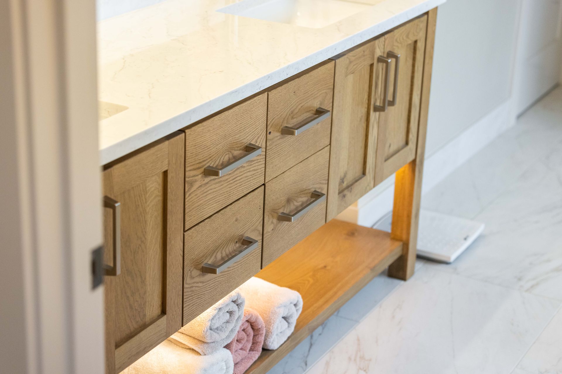 Wooden bathroom vanity with drawers, white countertop, and folded towels on the lower shelf