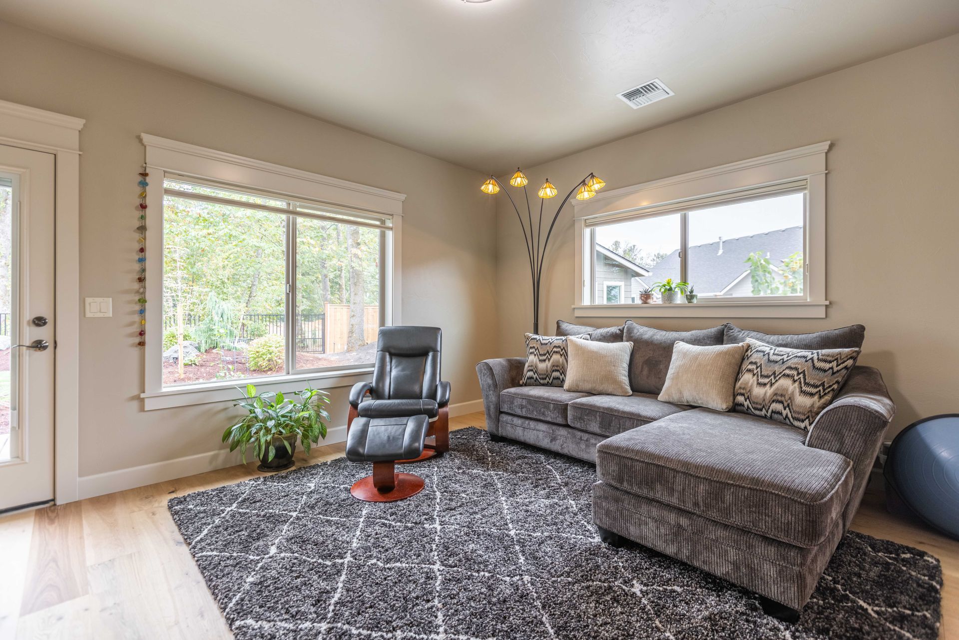 Bright living room with gray sectional, black chair, large windows, shag rug, and floor lamp