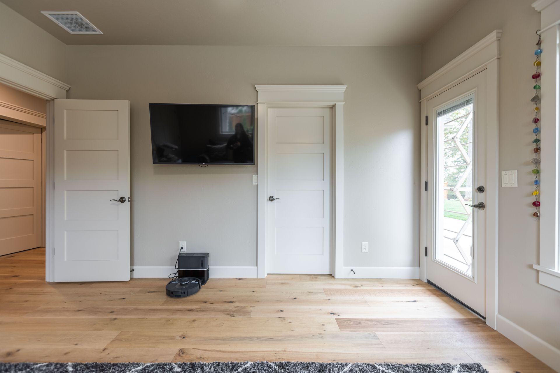 Empty room with wall-mounted TV, two white doors, and sliding glass door on light wood floors
