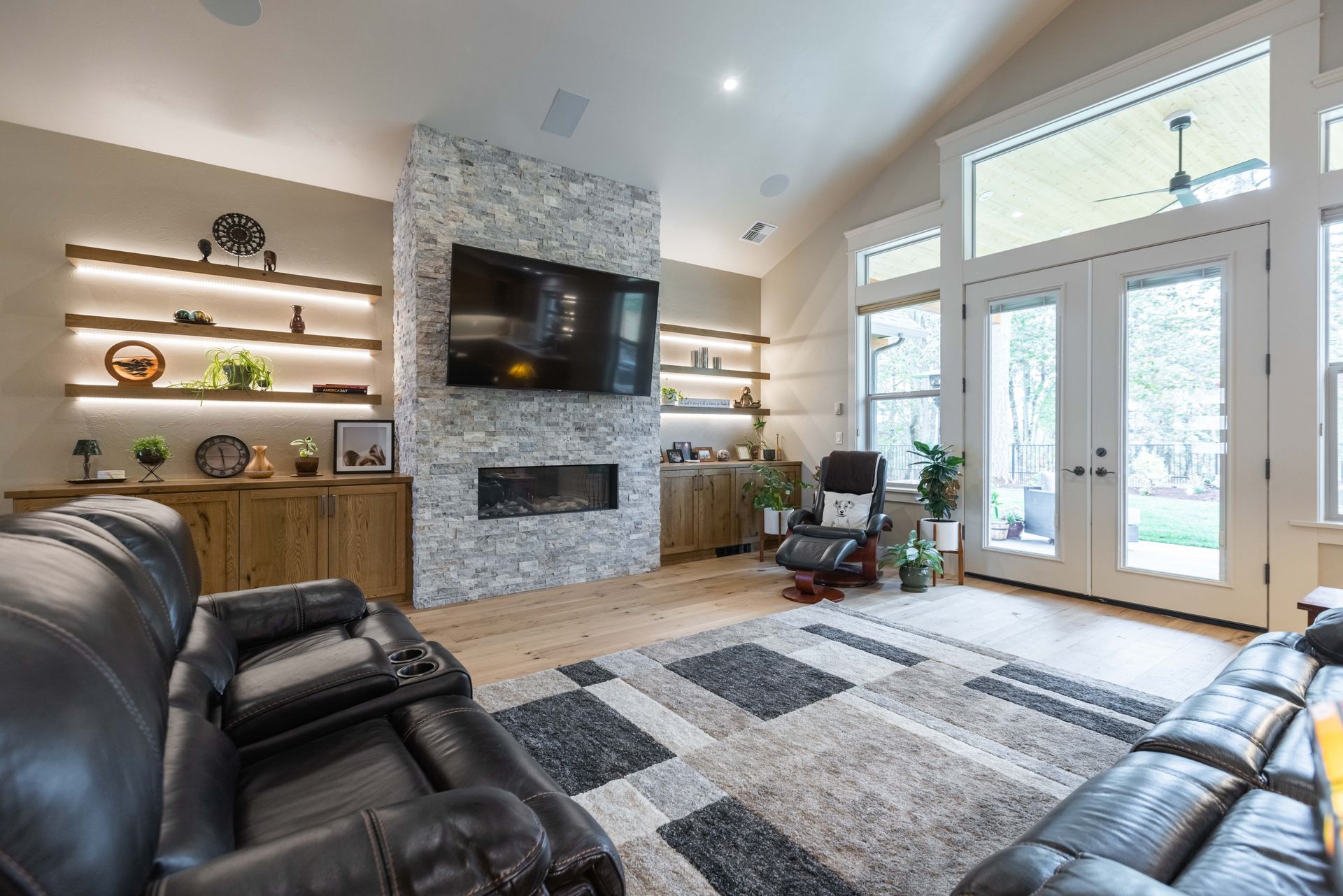 Modern living room with stone fireplace, wall TV, leather sofas, and large French doors