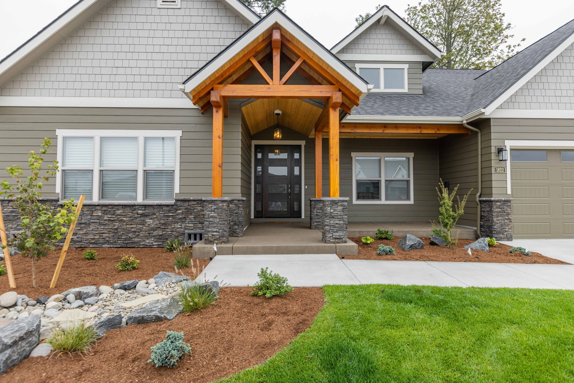 Modern house exterior with stone accents, gabled roof, front porch, and landscaped walkway.