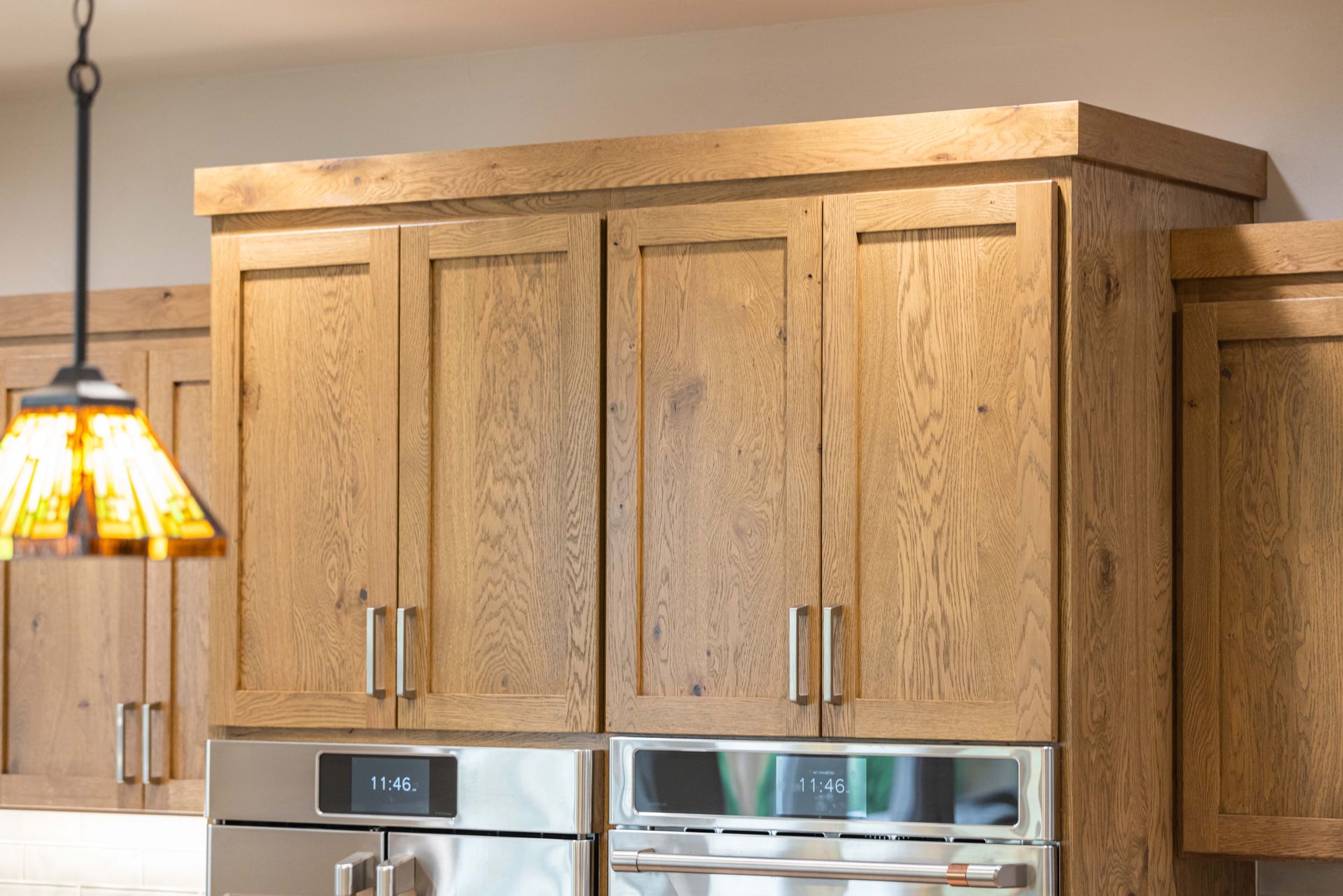 Wooden kitchen cabinets above stainless steel appliances, with a hanging stained-glass pendant light on the left.