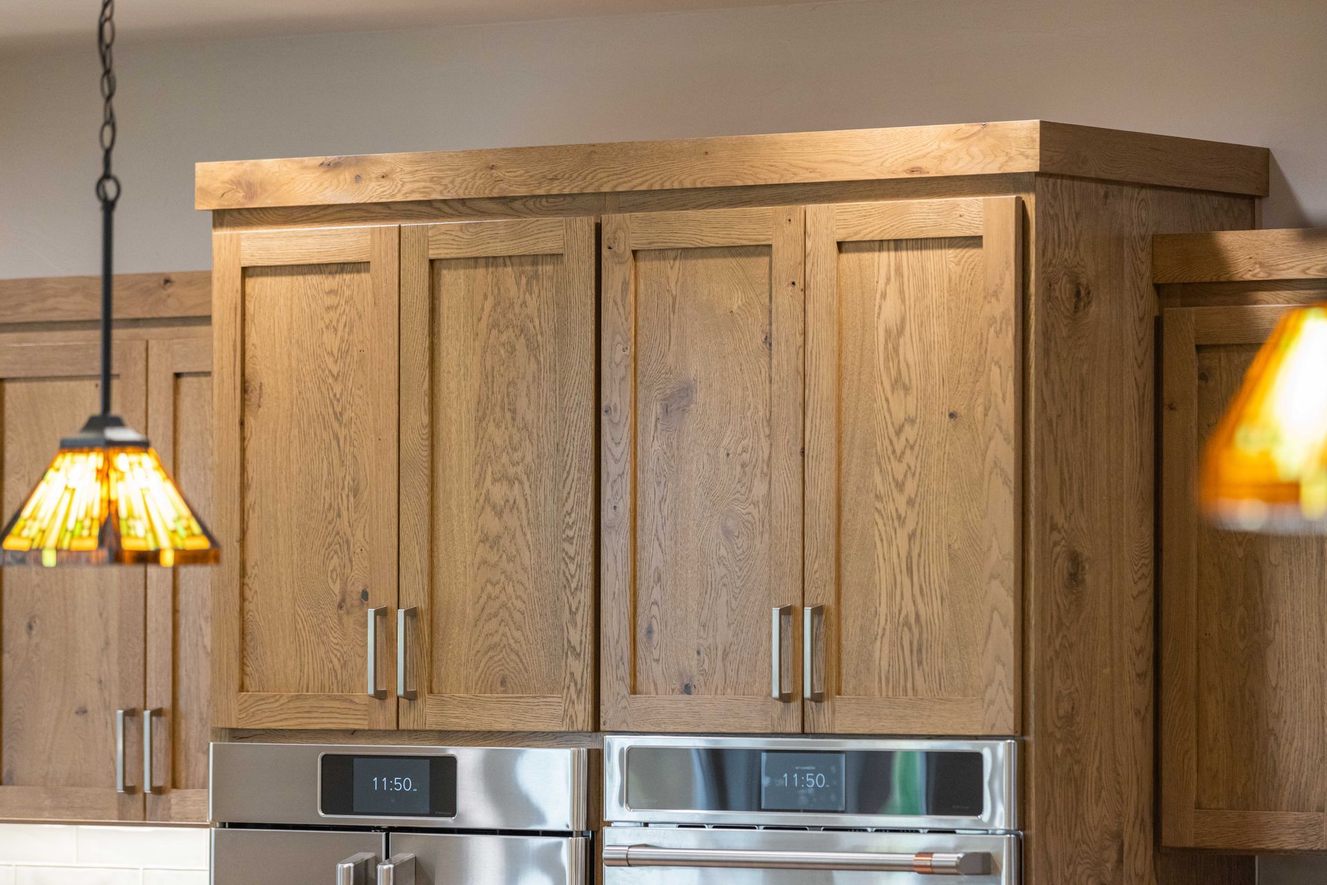 Wooden kitchen cabinets above stainless steel appliances with pendant lights in a warm interior