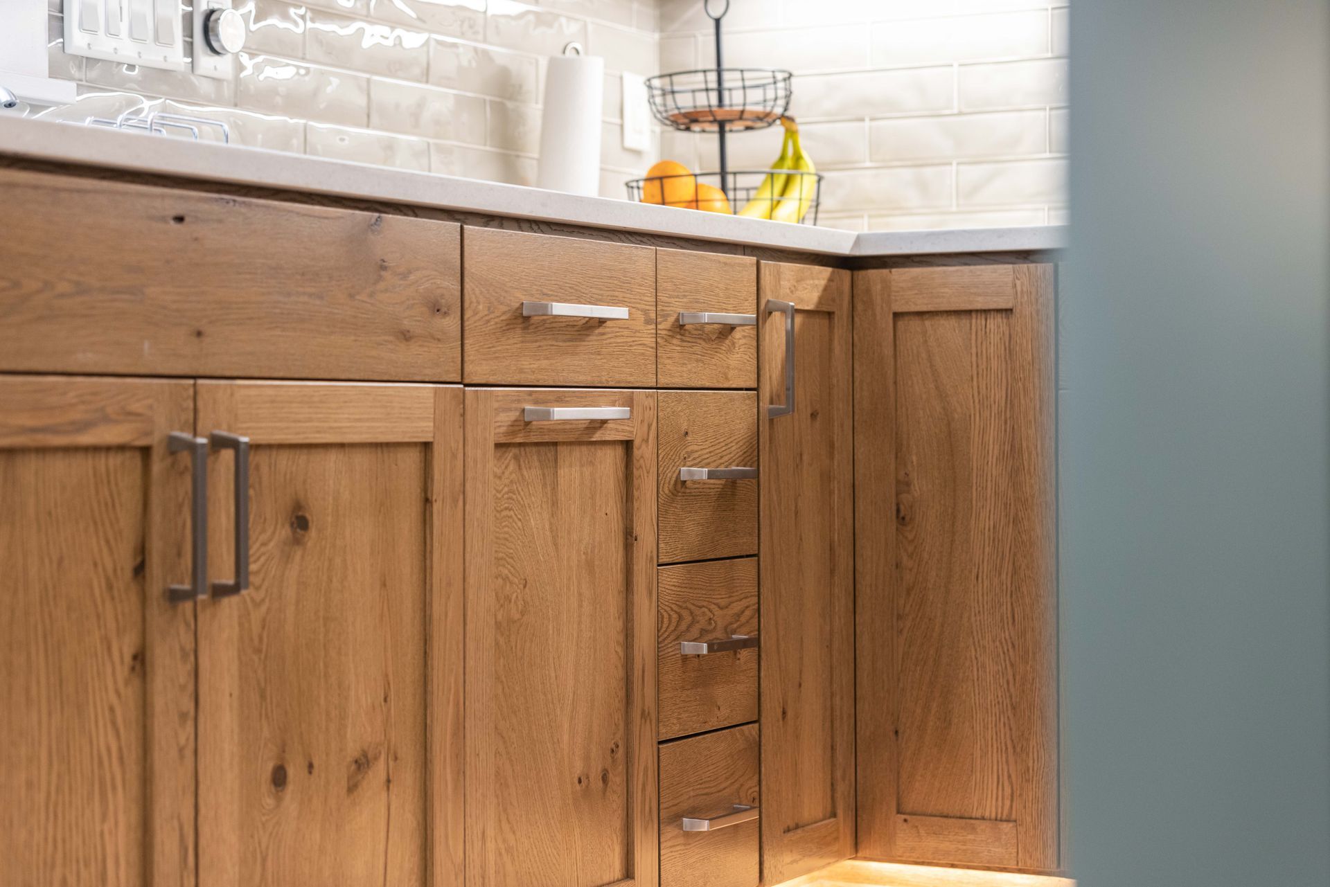 Wooden kitchen cabinets with drawers, stone countertop, and a fruit bowl on a white brick backsplash.