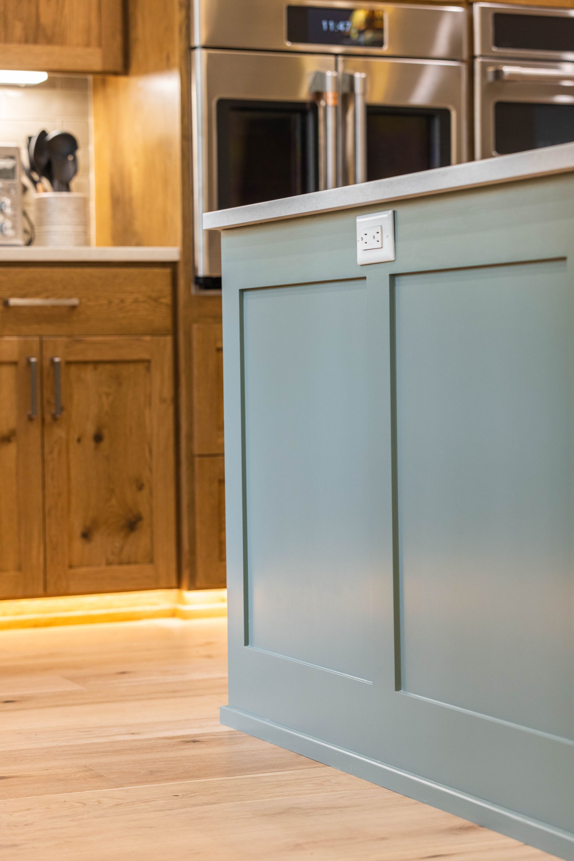 Kitchen island with blue paneling and white countertop beside wood cabinets and built-in ovens