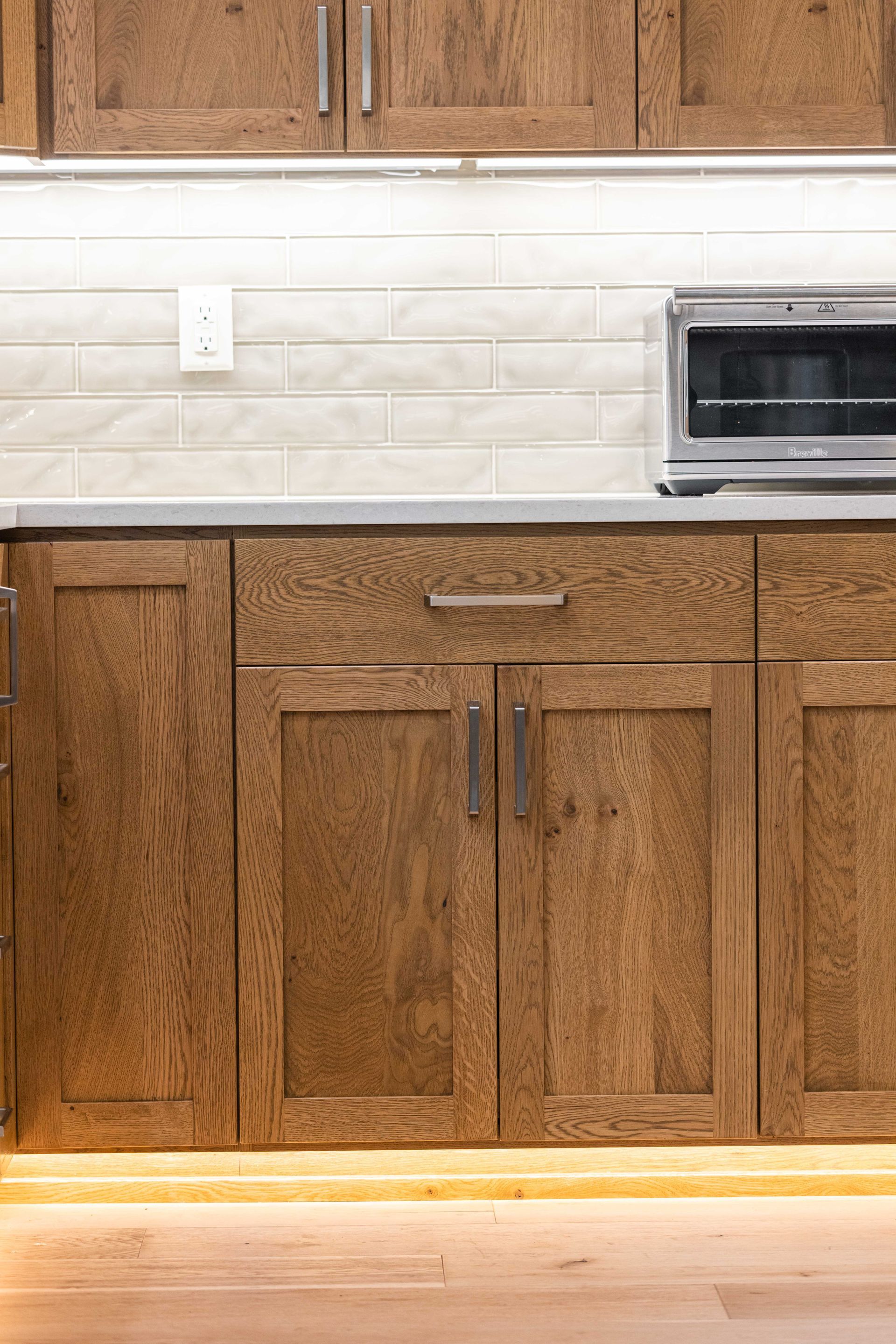 Kitchen cabinets and countertop with white tile backsplash and a toaster oven on the right.