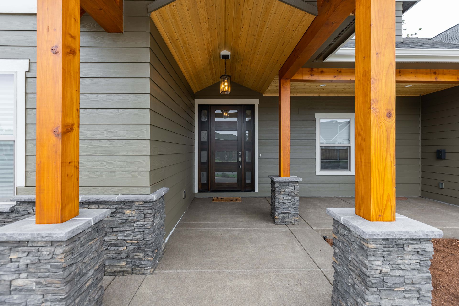 Covered front porch with stone columns and a glass entry door on a house