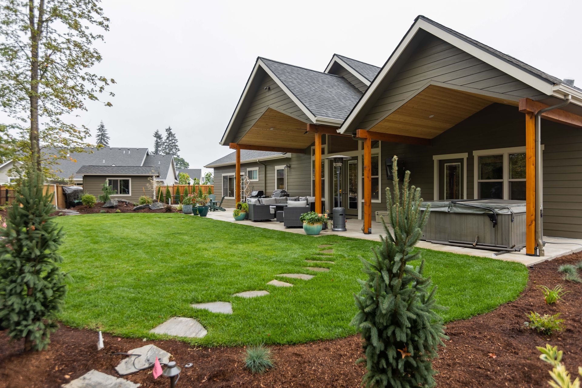 Modern house with wood porch and stone path beside a green lawn in a landscaped backyard