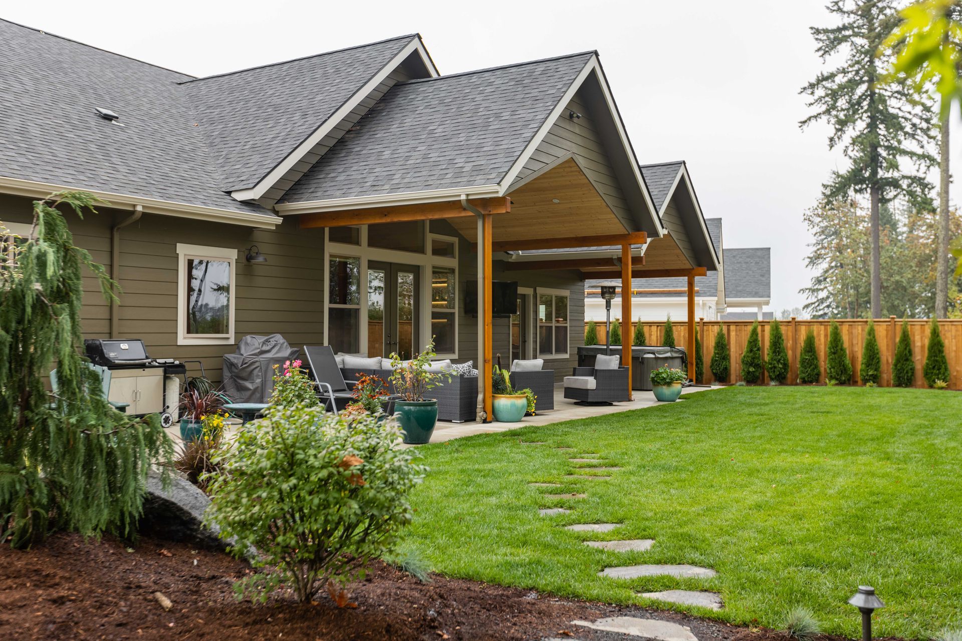 Backyard patio with gray house, covered seating, green lawn, and stepping stones