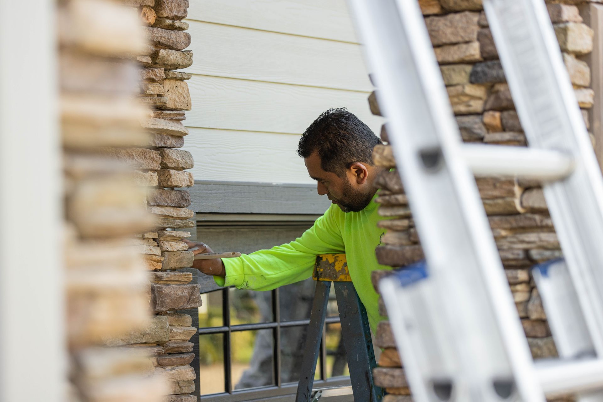 Worker in a neon green shirt installing a railing beside a stone house.