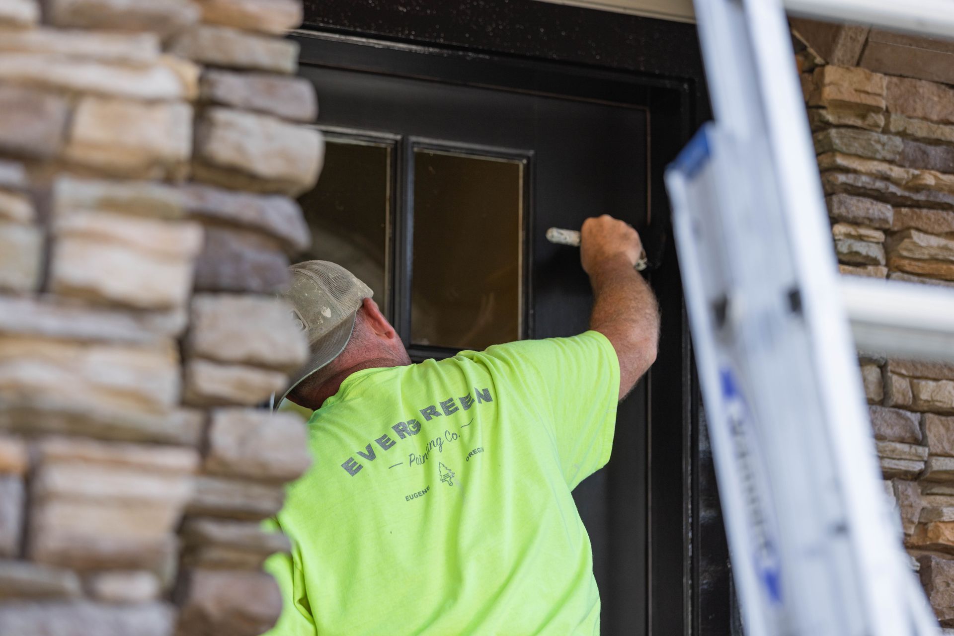 Worker in neon yellow shirt installing a dark door beside a stone wall
