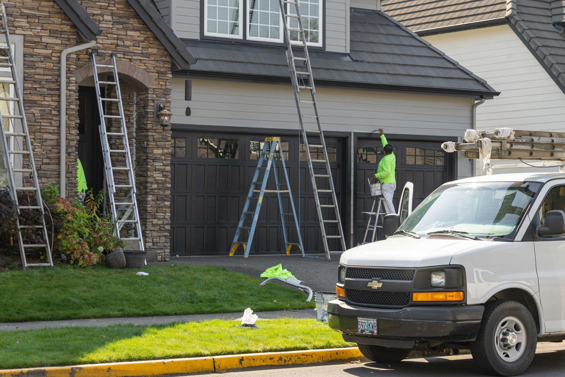 Workers on ladders repairing a house exterior and garage in a suburban driveway