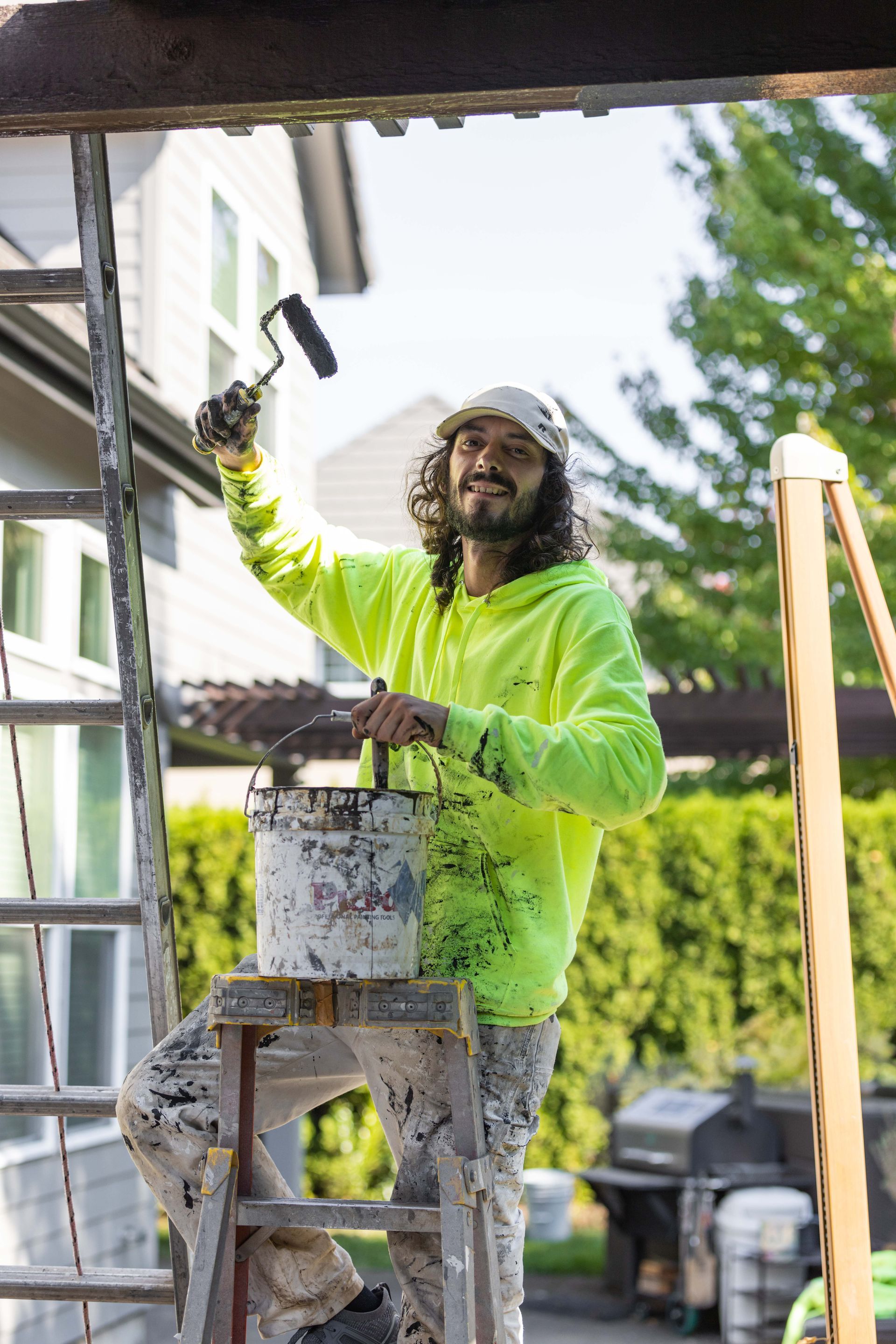Painter in a neon green shirt painting an outdoor house trim on a ladder