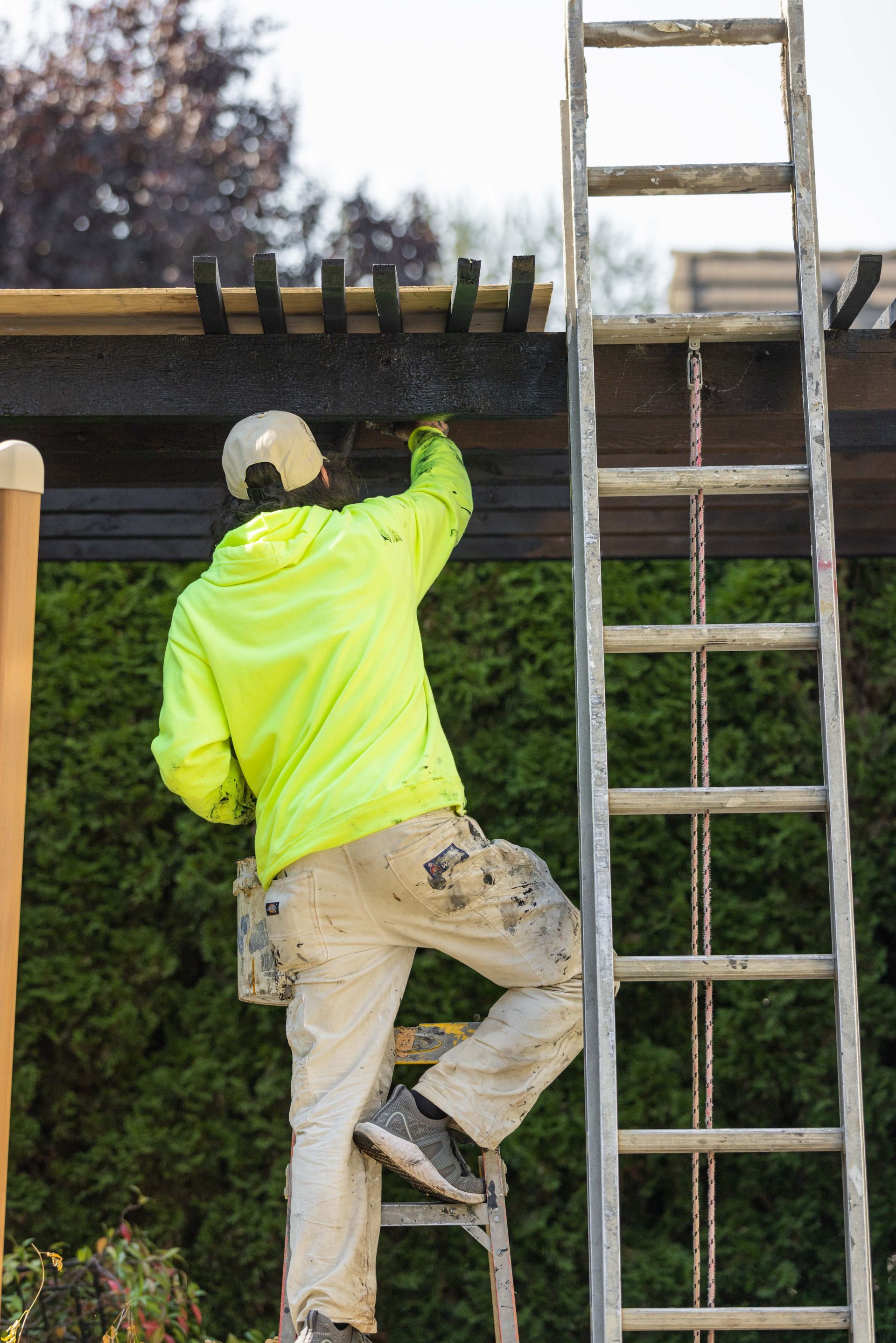 Worker in neon jacket climbs a ladder to fix a roof on a building.