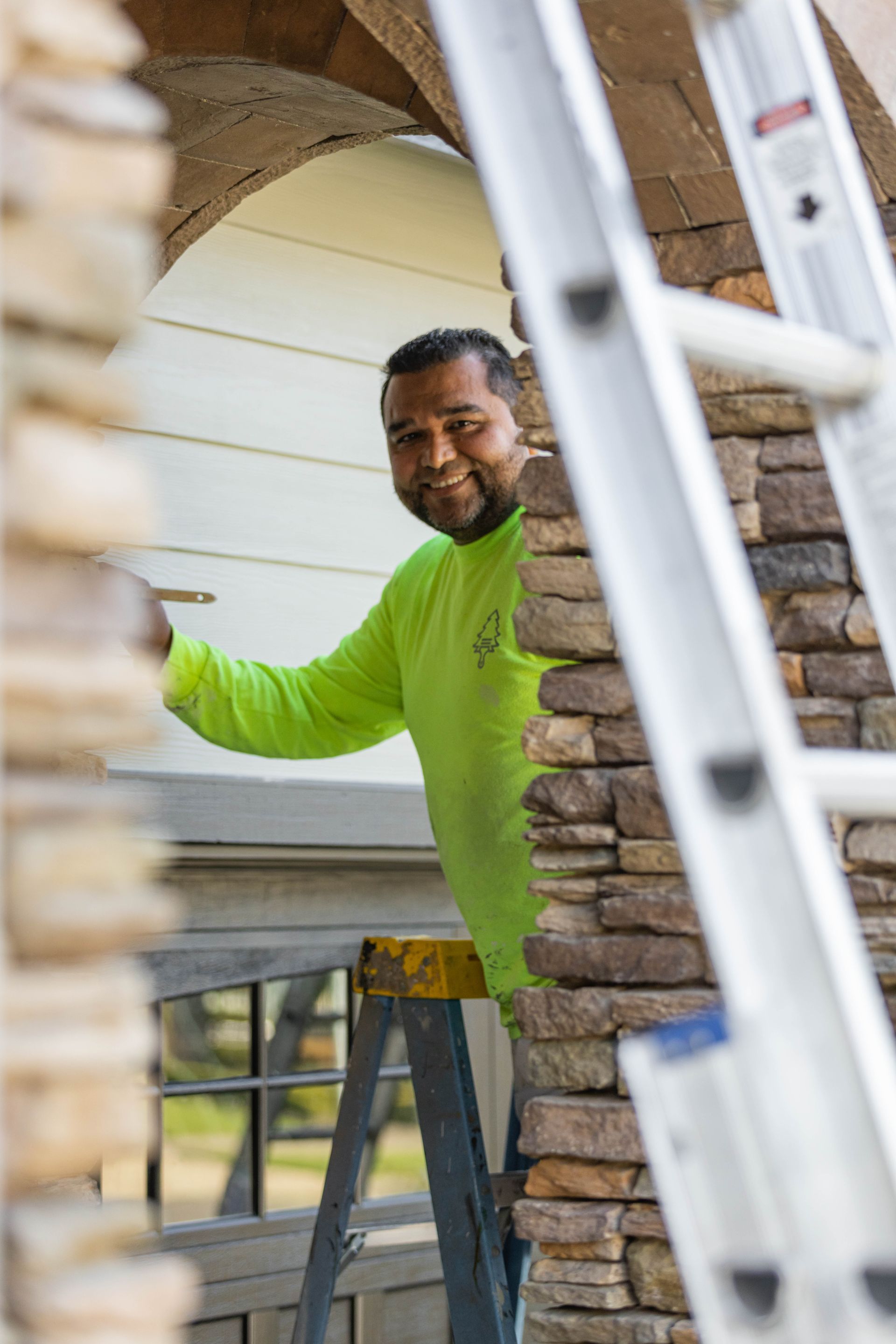 Worker in a neon green shirt standing on a ladder during home repair