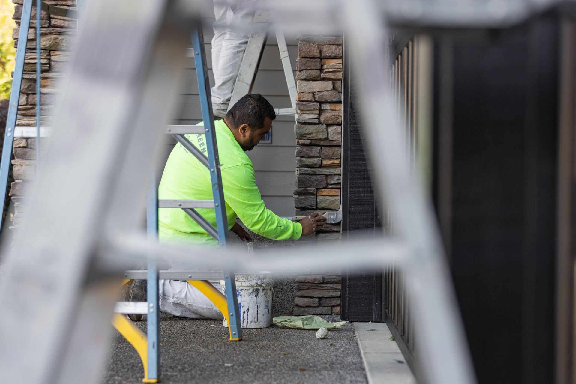 Worker in a neon jacket kneeling by a stone wall, using tools during construction.