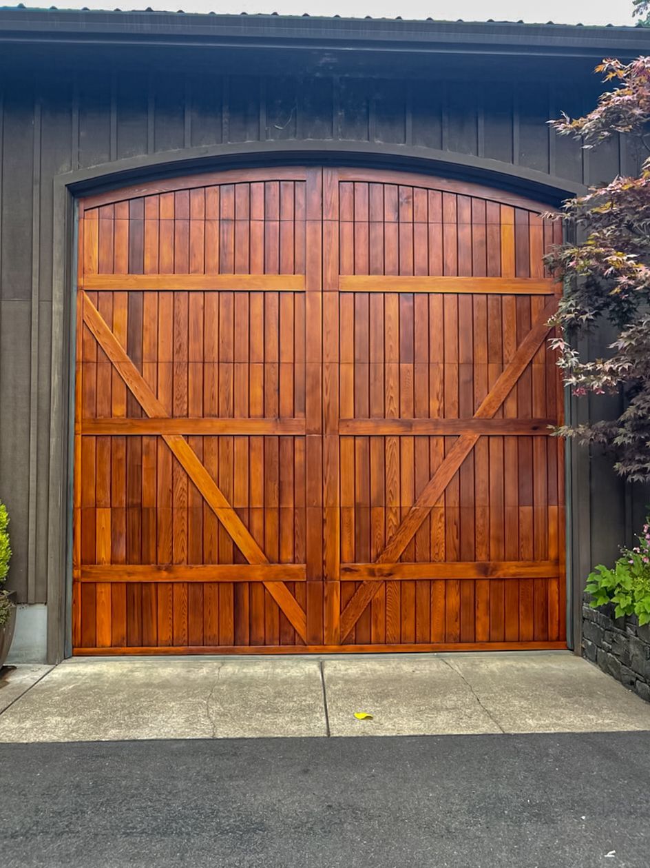 Wooden double garage doors on a dark exterior wall, framed by concrete and black asphalt.