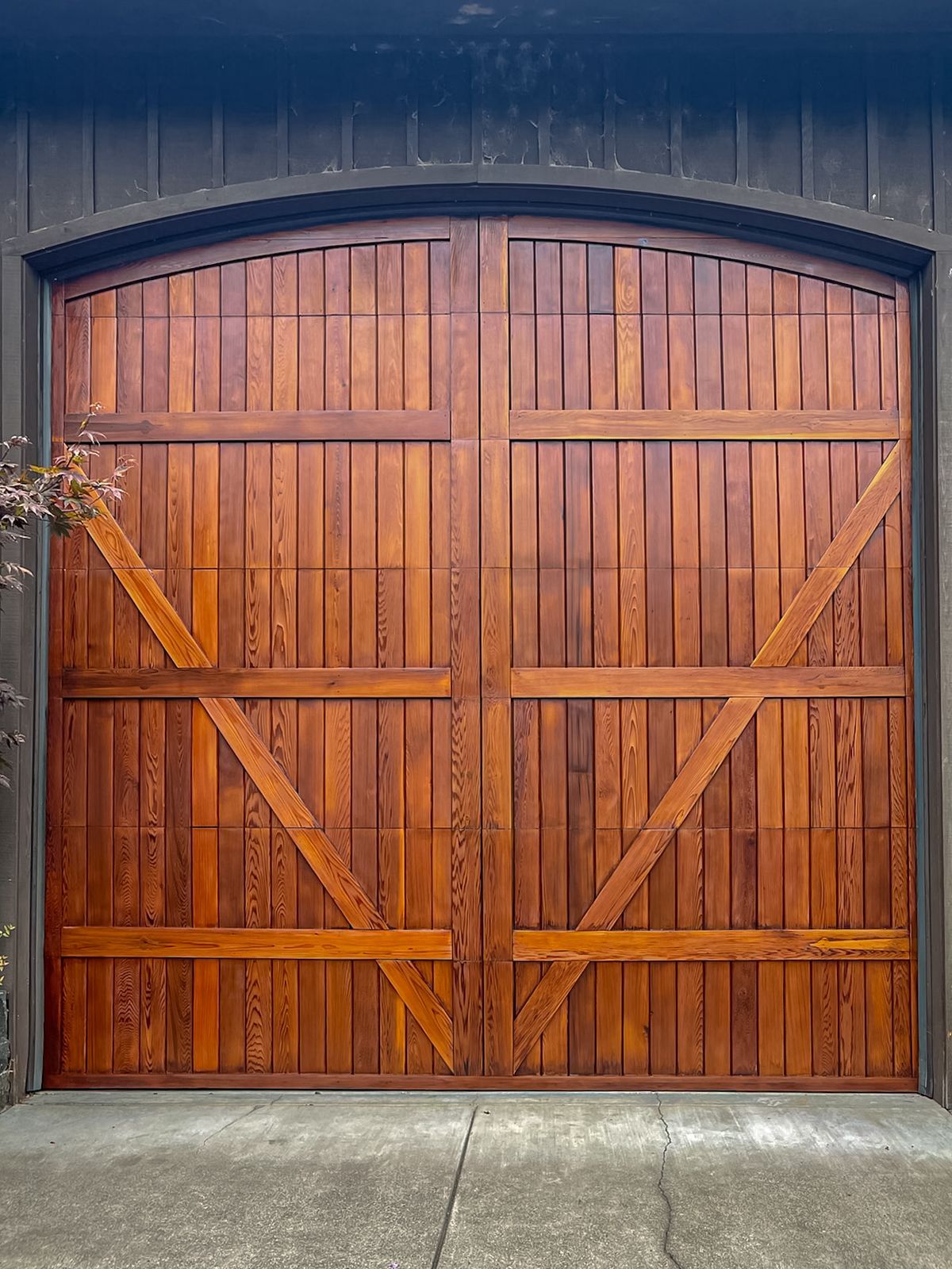 Wooden double barn doors with arched top and diagonal braces in a stone wall opening