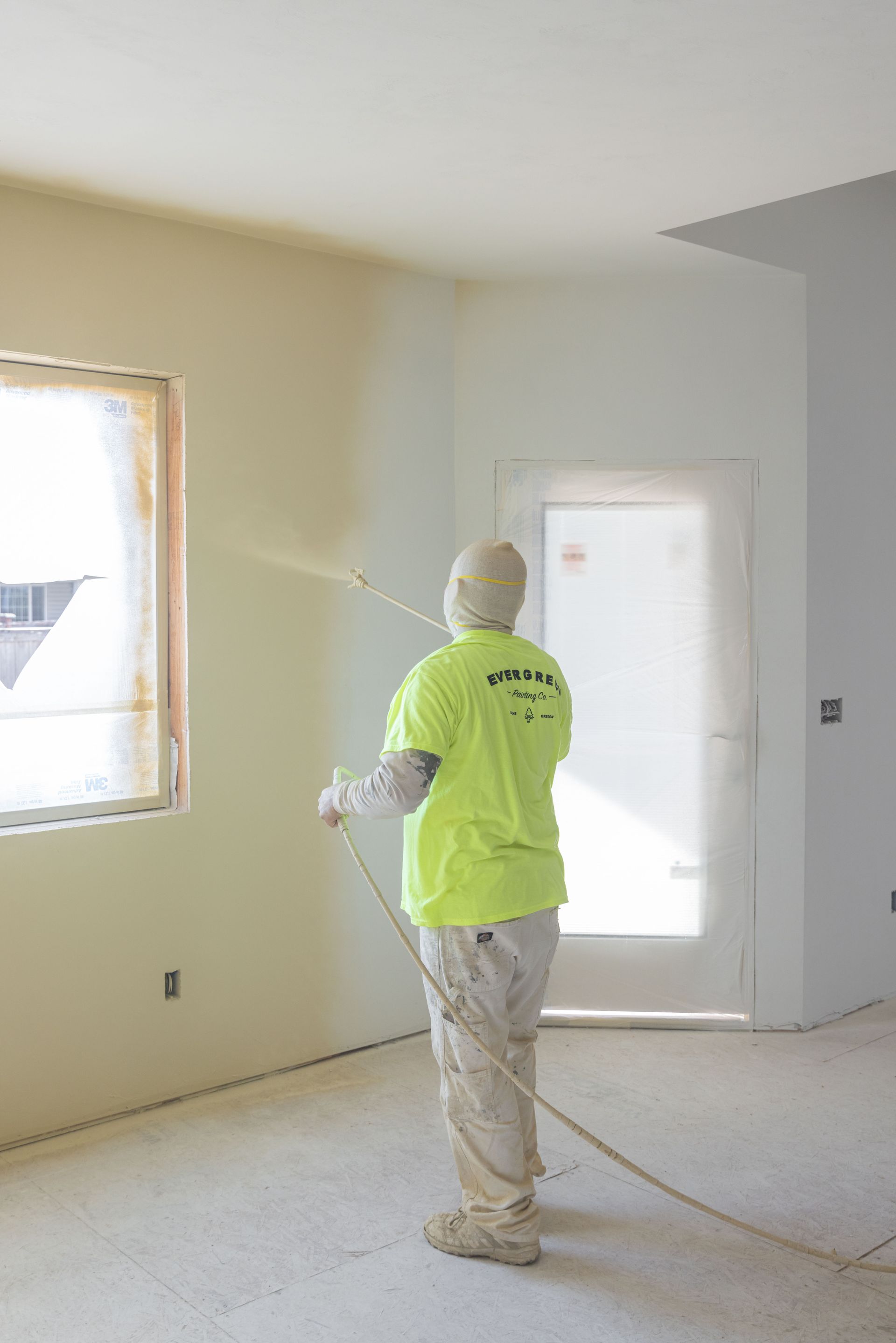 Worker in neon yellow shirt spray-paints interior walls of a room under renovation.