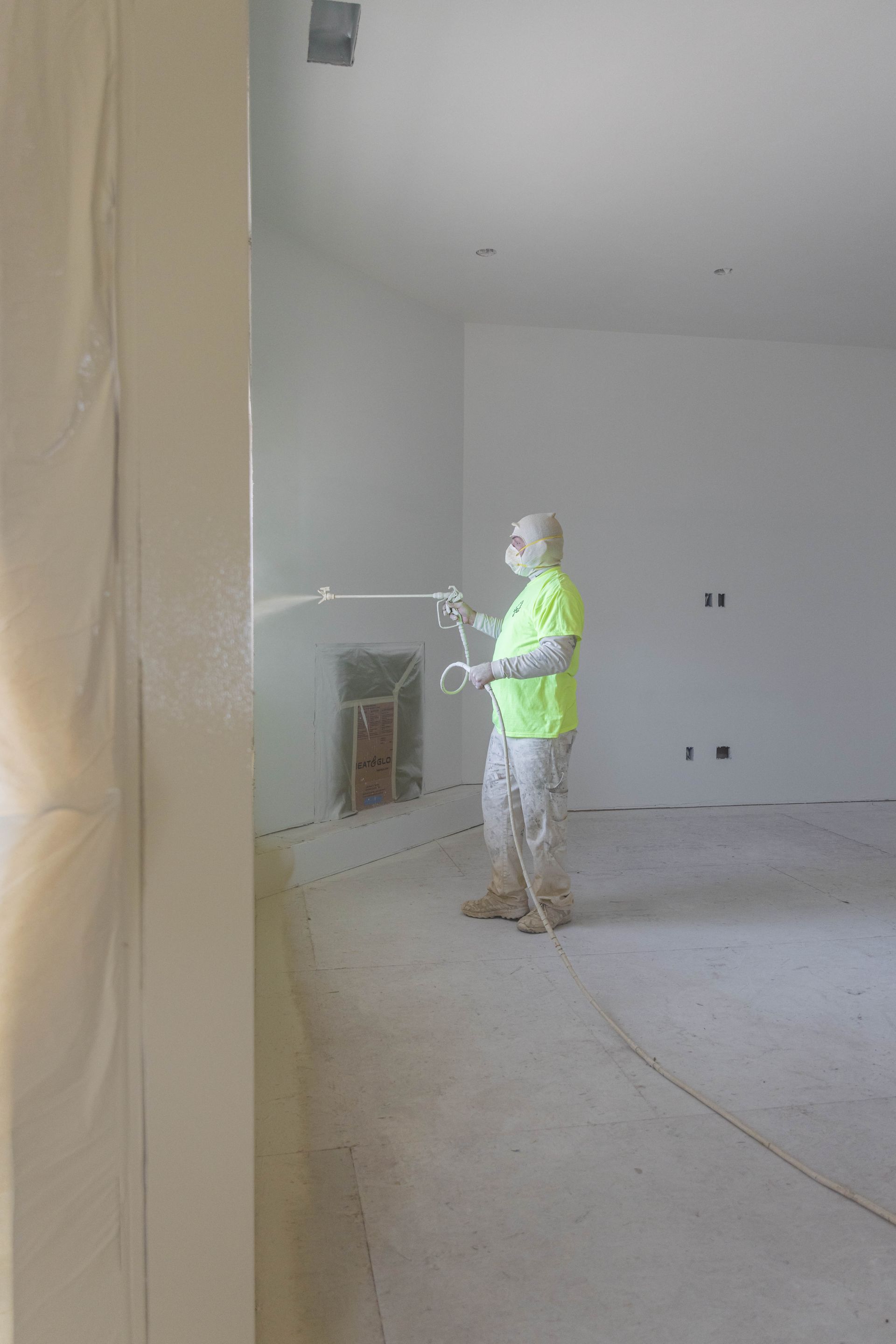 Worker in neon vest painting a wall inside an unfinished room.